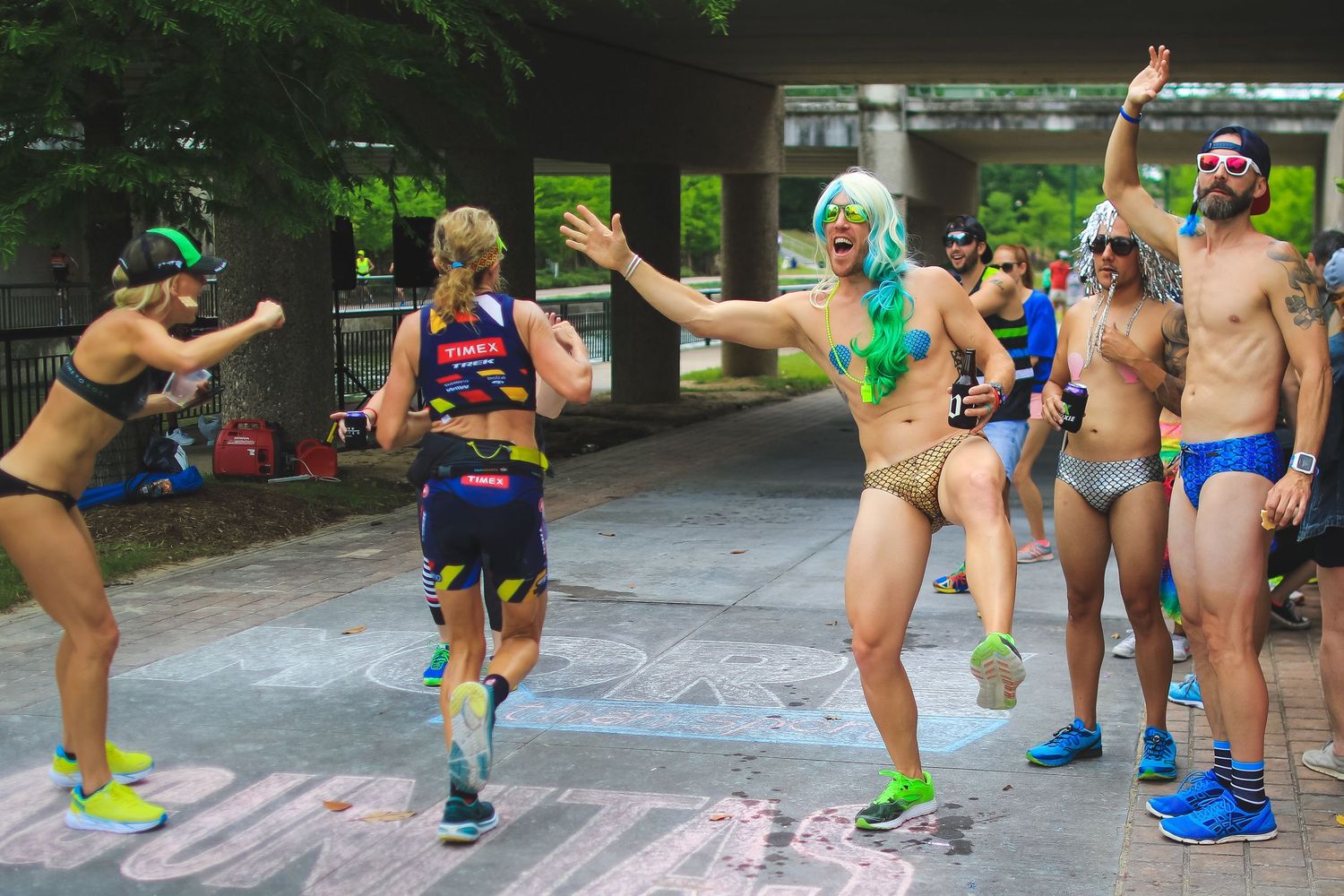 Colorful group of runners and spectators dancing and cheering during outdoor race event.