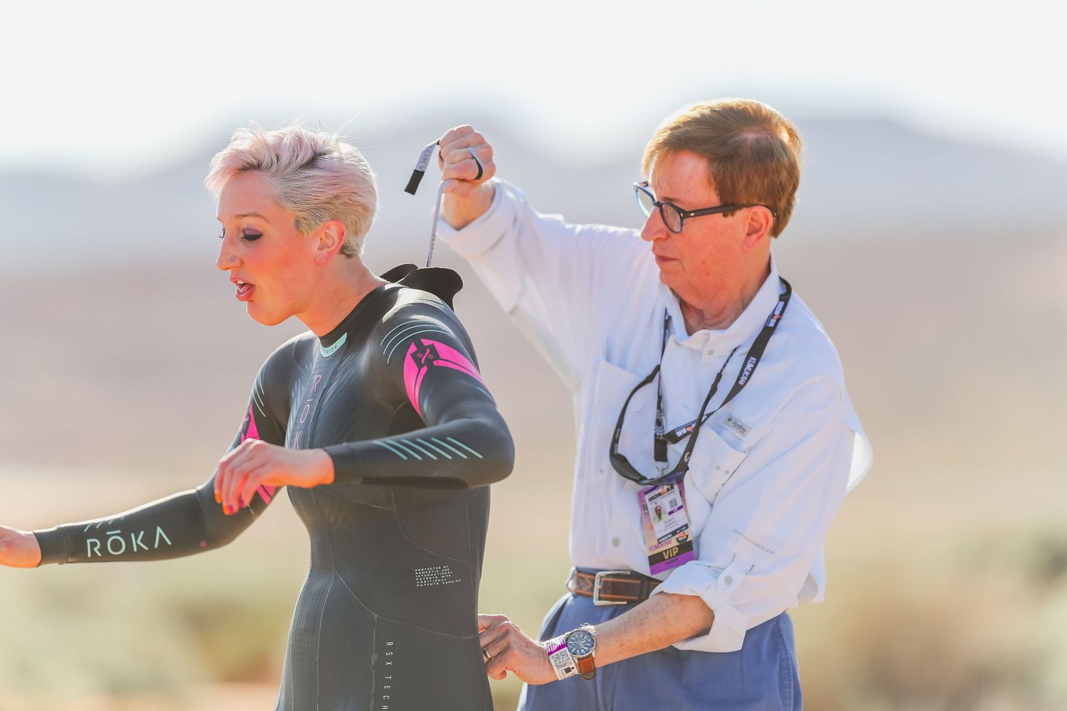 Race official helps female triathlete zip up her ROKA wetsuit before competition start.