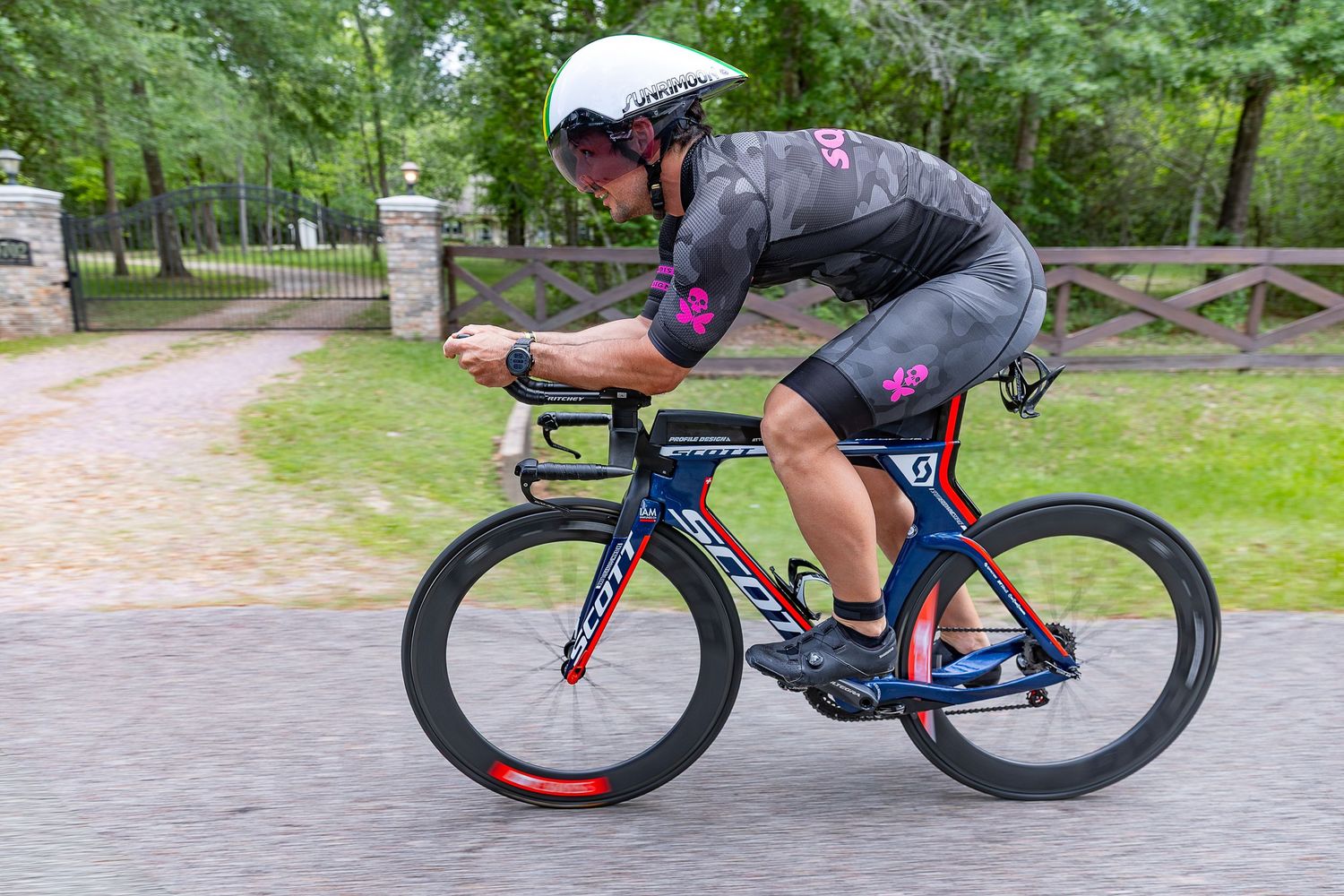 Cyclist in aerodynamic position racing on Scott triathlon bike wearing gray and pink kit with helmet.