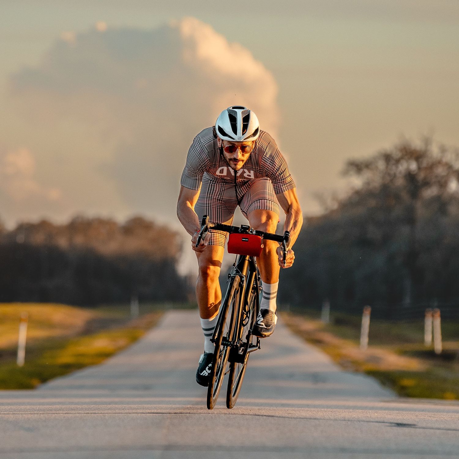 Cyclist in racing gear riding road bike on open highway at golden hour sunset.