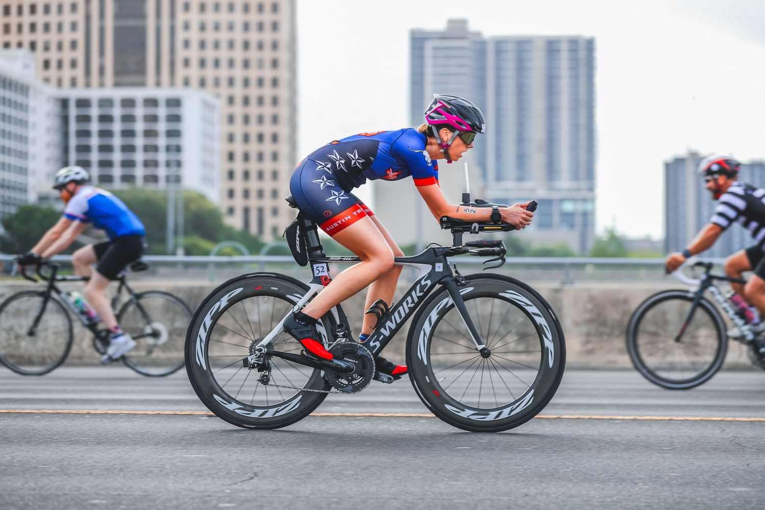Female cyclist racing on triathlon bike through urban city bridge course.