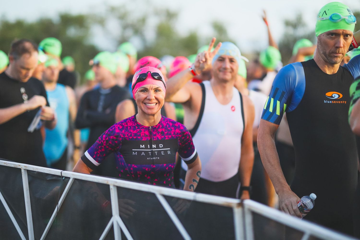 Smiling female triathlete in pink swim cap waits at race start with competitors.