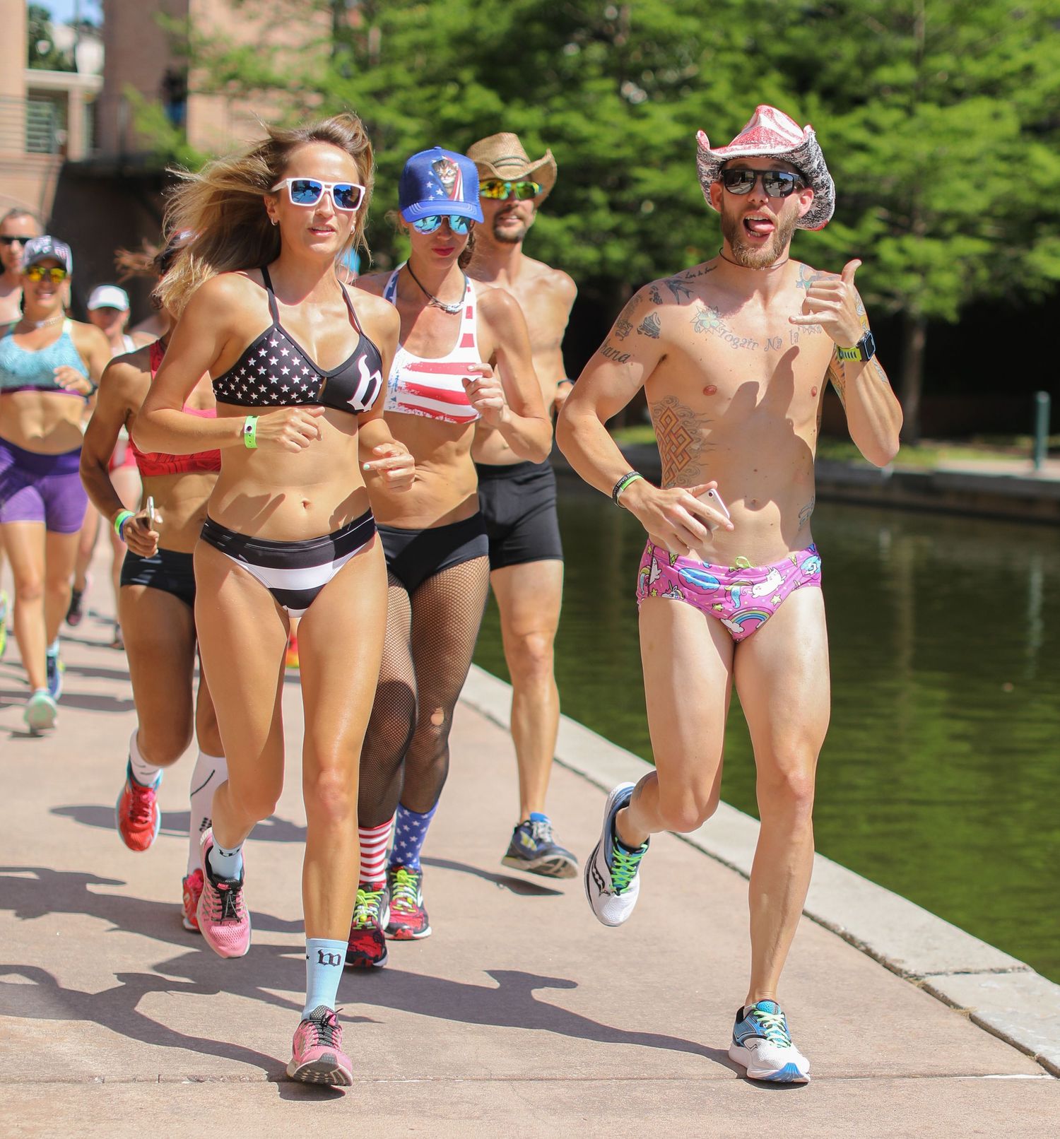 Athletes in patriotic swimwear and costumes running along a waterway during the .IMTX Underpants Run