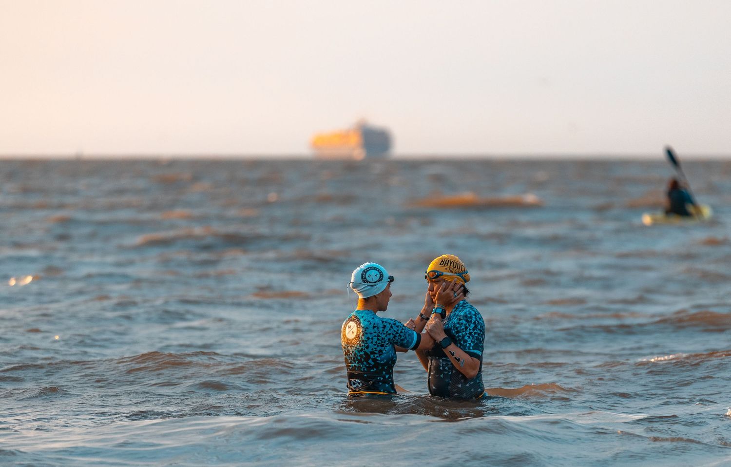 Two open water swimmers in caps pausing together in ocean at sunset.