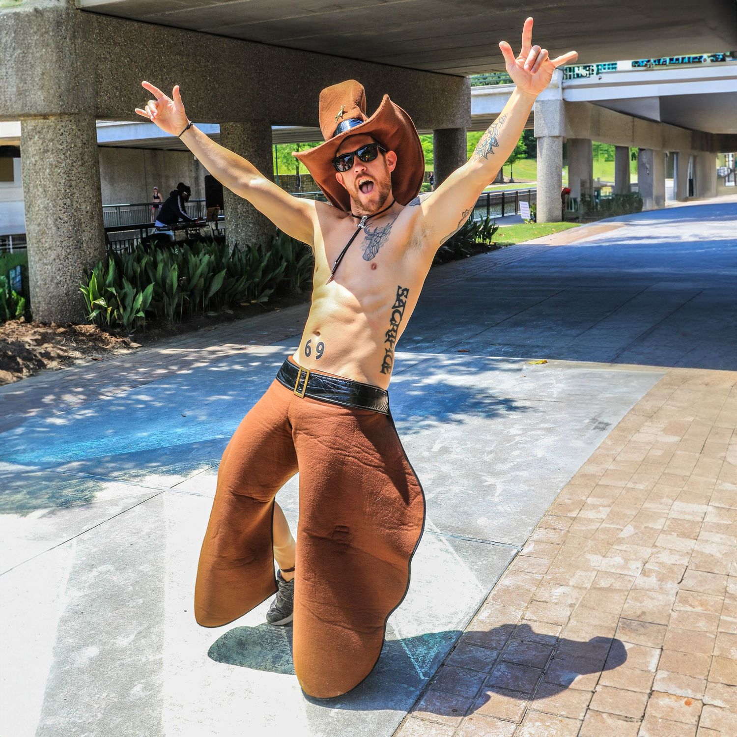 Shirtless man in cowboy hat and inflatable horse costume celebrates outdoors joyfully.