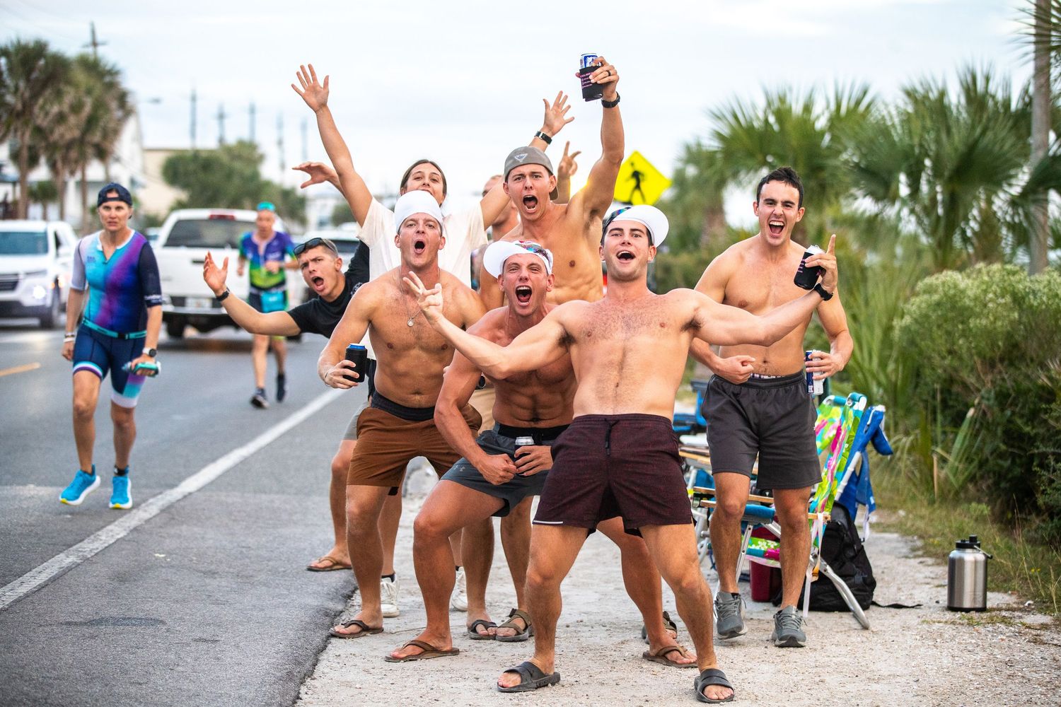 Group of shirtless men cheering and celebrating on roadside at triathlon event.