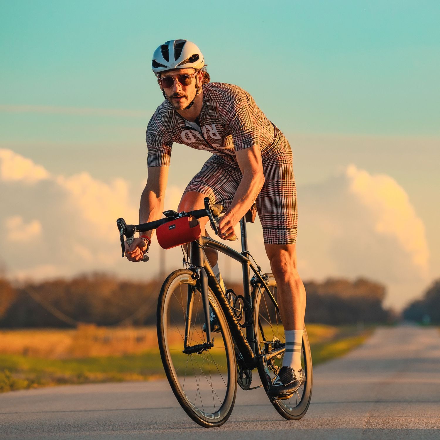 Male cyclist riding road bike in checkered kit on open highway.