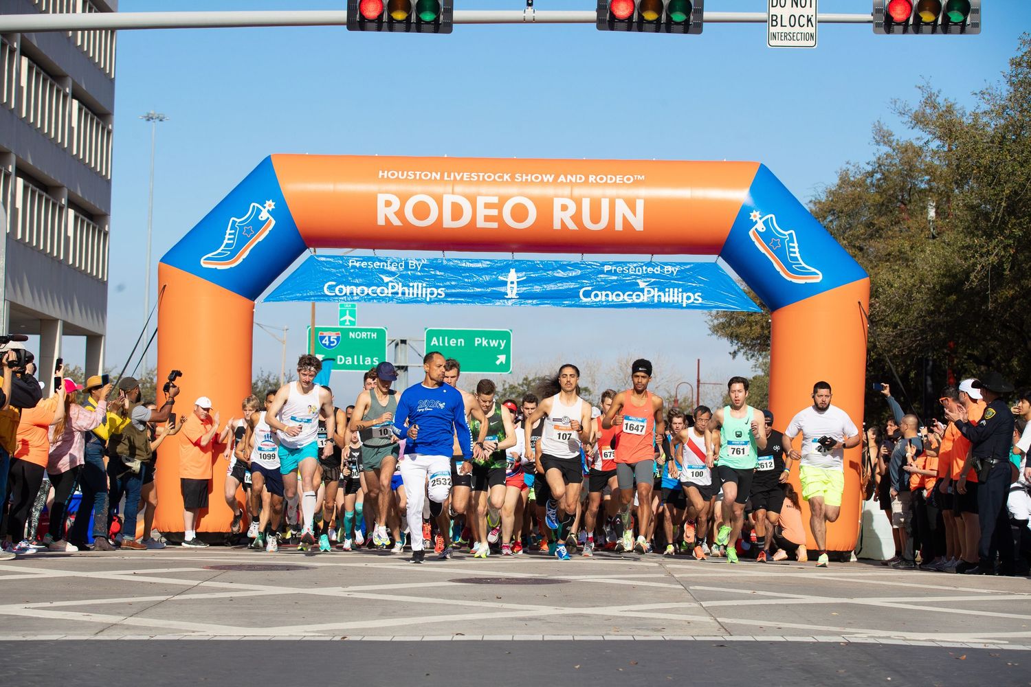 Large crowd of runners starting the Rodeo Run race under an orange inflatable arch sponsored by ConocoPhillips.