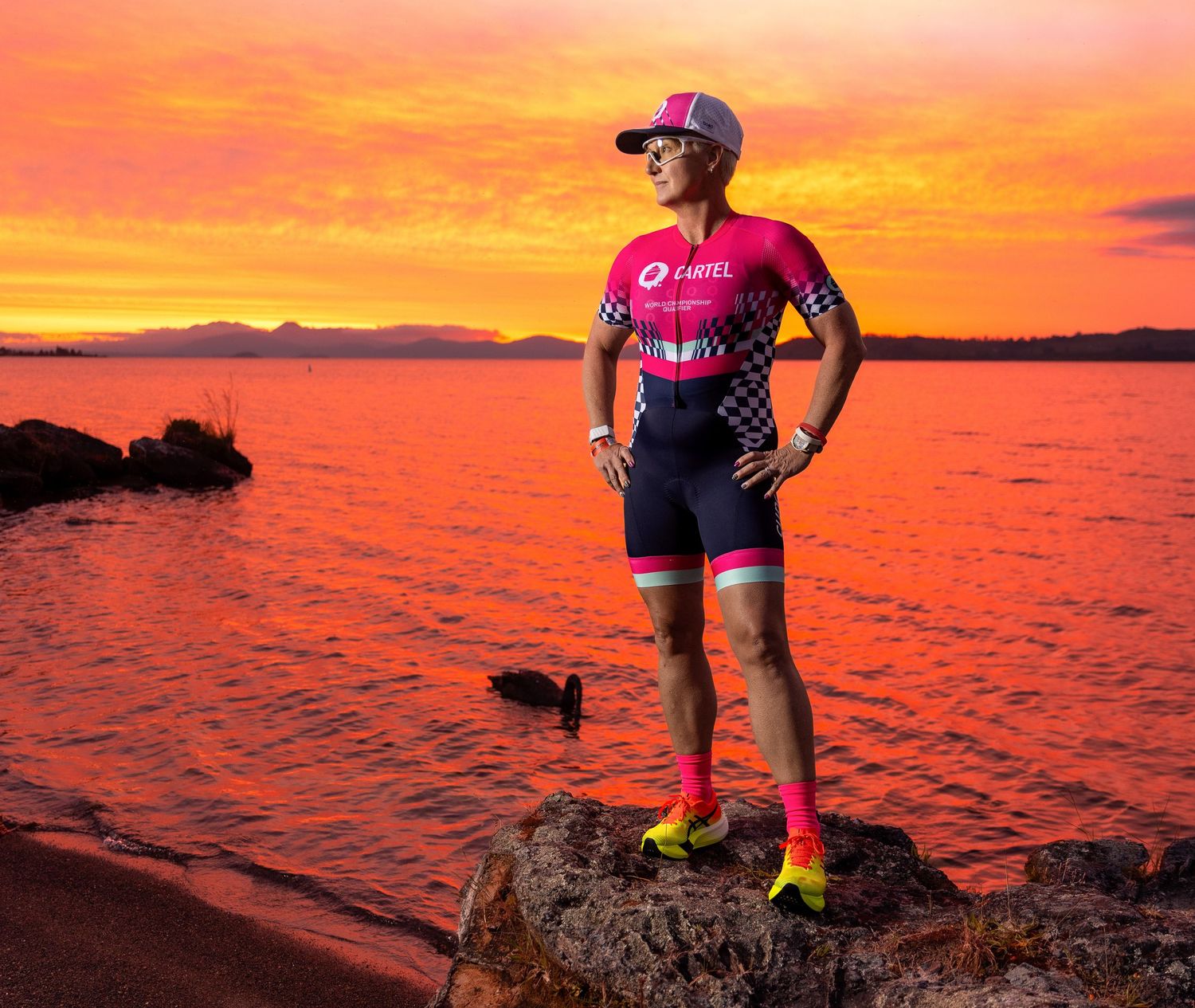 Triathlete standing on lava rocks at sunset in Taupō, New Zealand during an endurance sports portrait session.