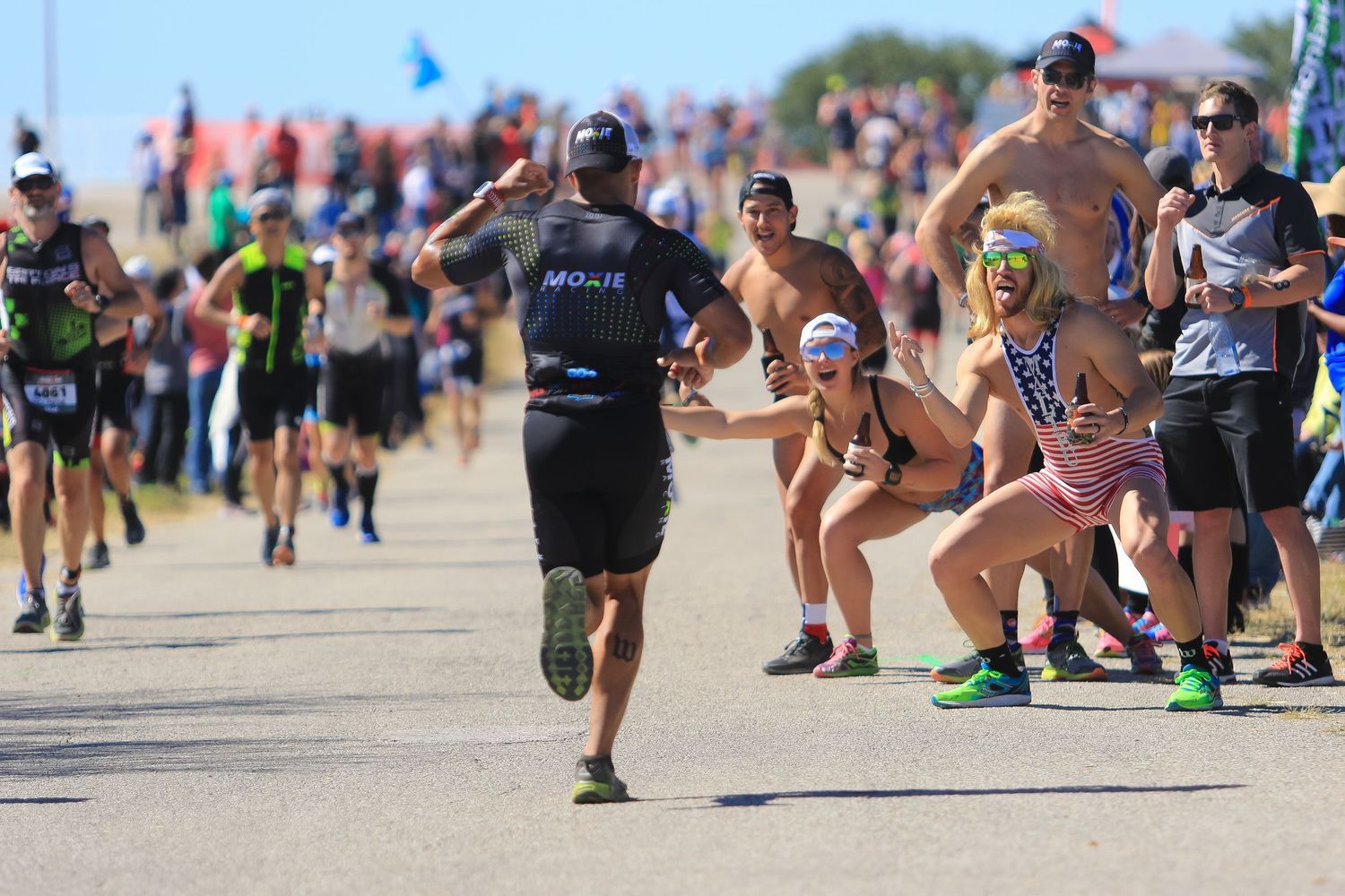 Runners and costumed spectators interact energetically along sunny triathlon race course.