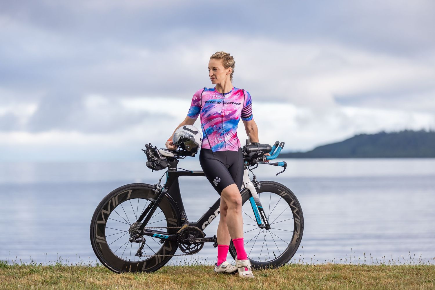 Female triathlete portrait beside Cervélo triathlon bike on a lakeshore during an endurance sports photoshoot in Taupō, New Zealand.