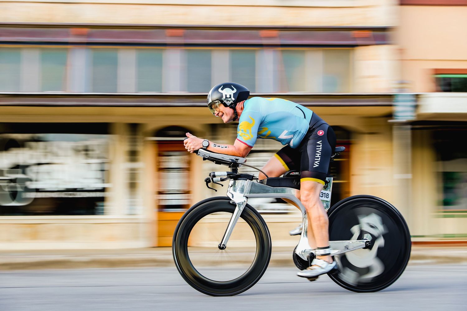 Cyclist in colorful kit riding time trial bike through town at speed.