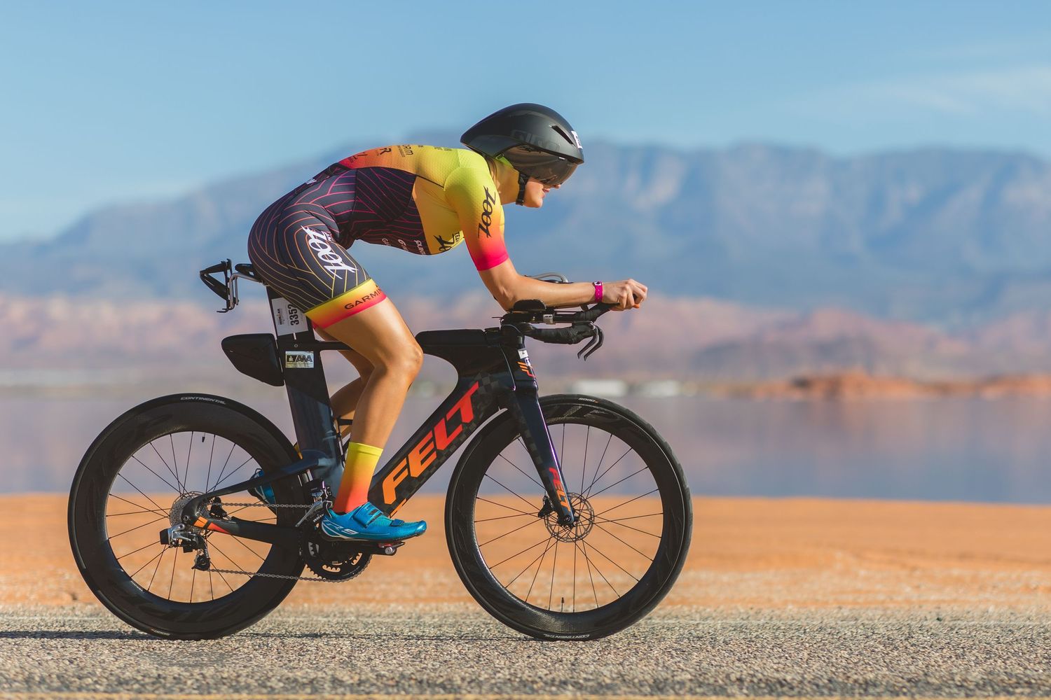 Triathlete racing on Felt bike in colorful kit with desert landscape.