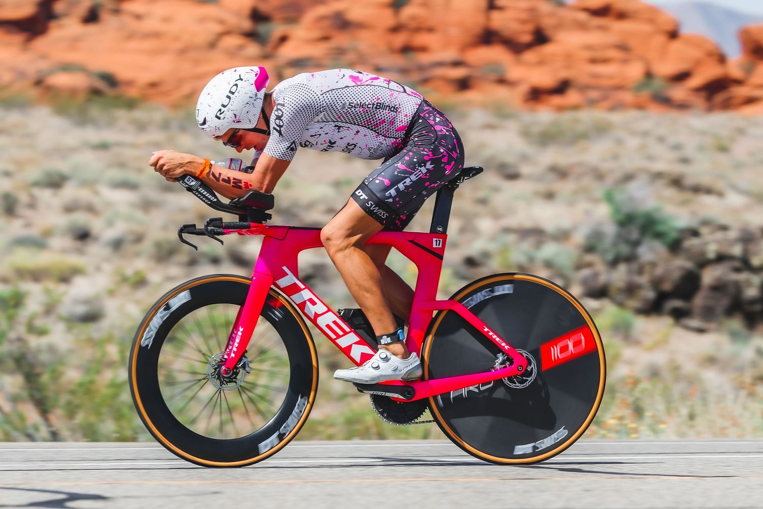Female cyclist rides a pink Trek time trial bike through a scenic red rock desert landscape.