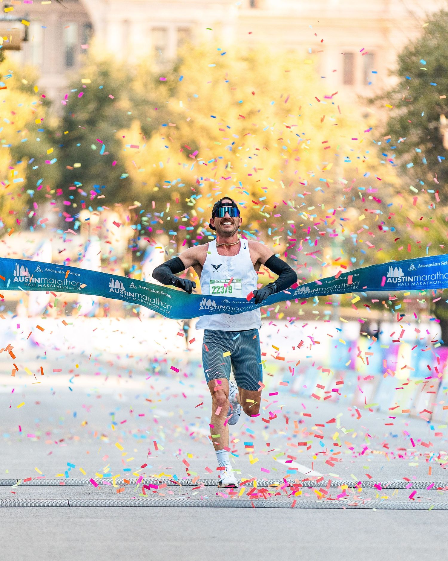 Male runner breaking finish line tape at Austin Marathon with confetti.