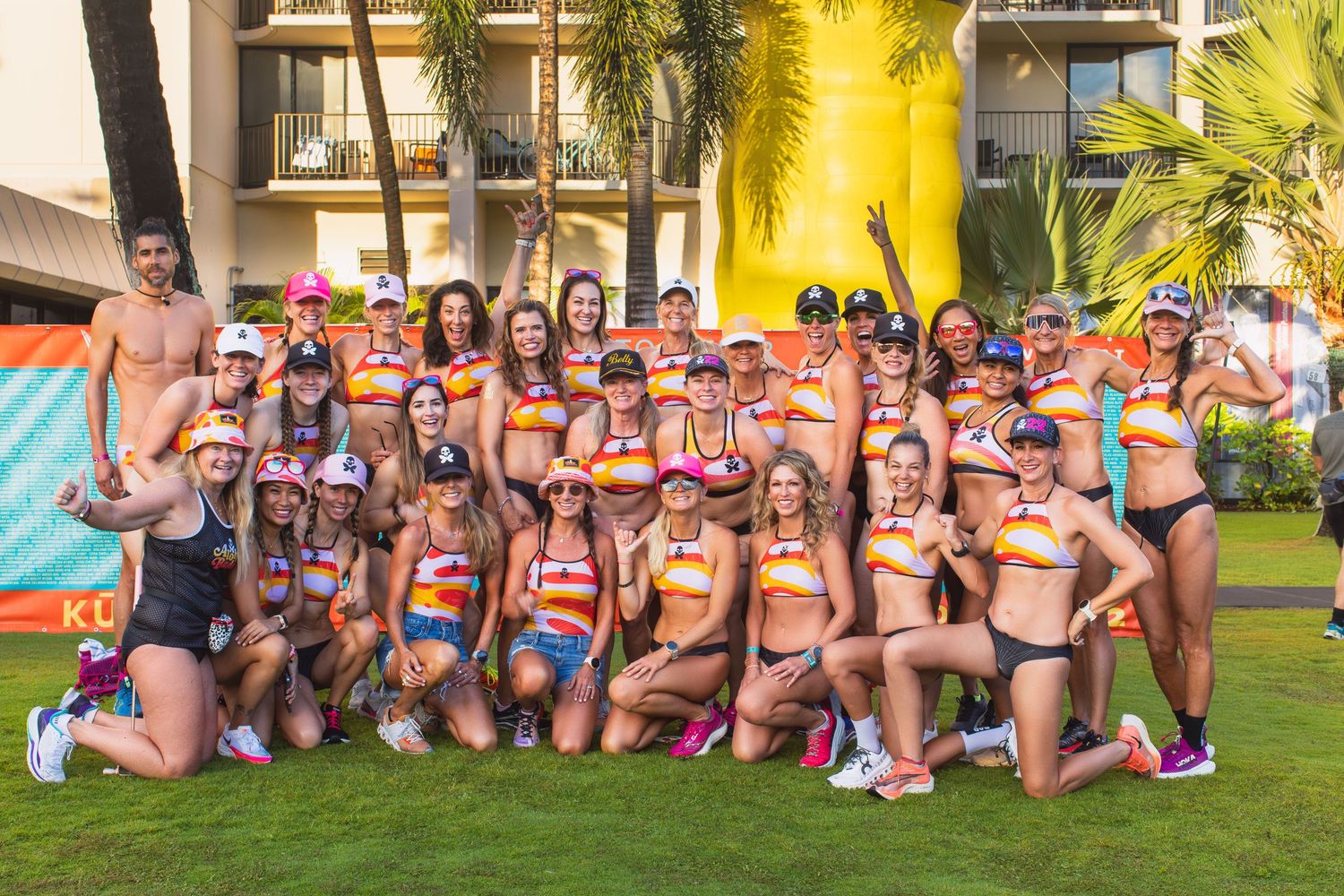 Large group of athletes in matching colorful triathlon kits posing together on a hotel lawn at the Kona Underpants Run.