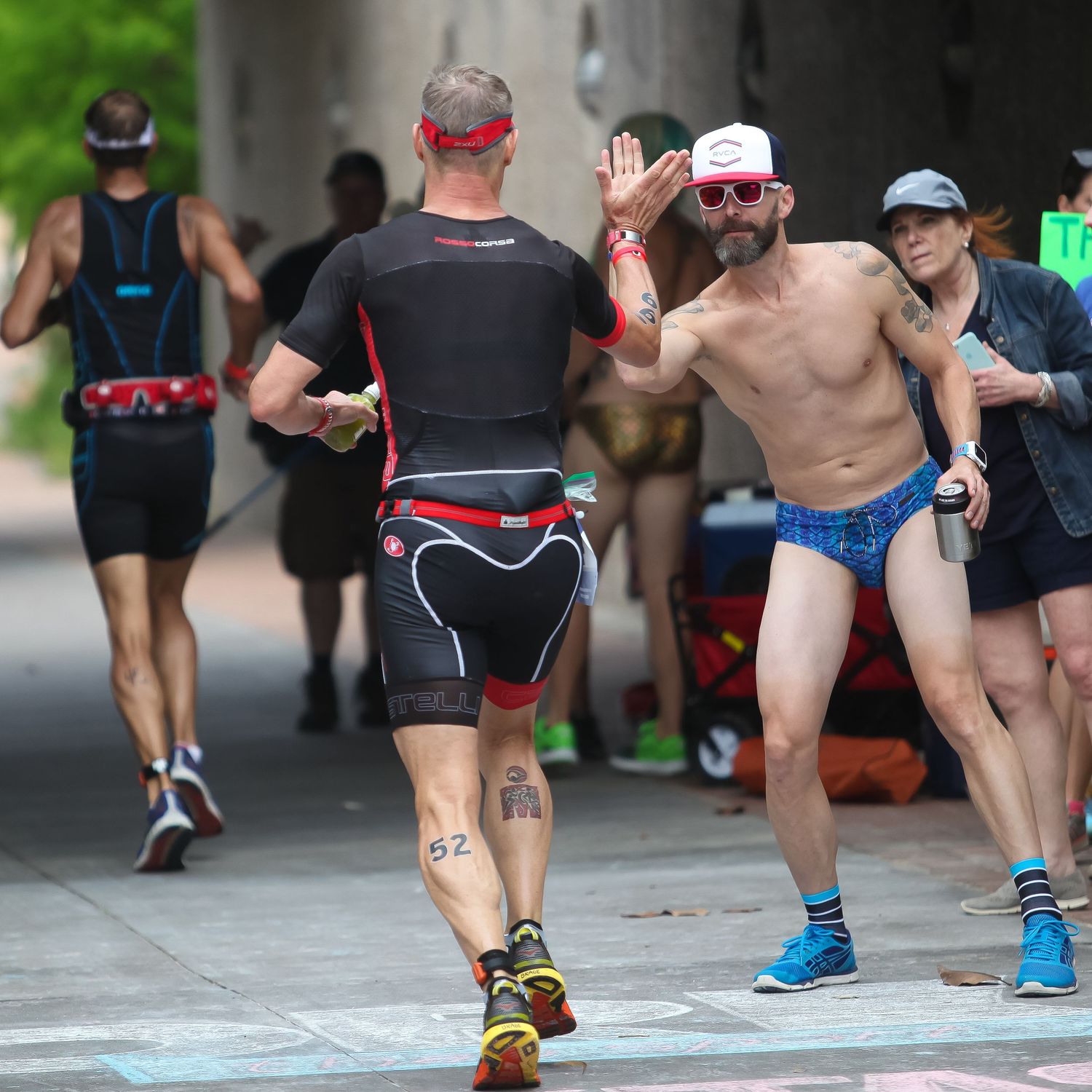 Two shirtless male triathlon runners high-fiving during a race event on a city street.