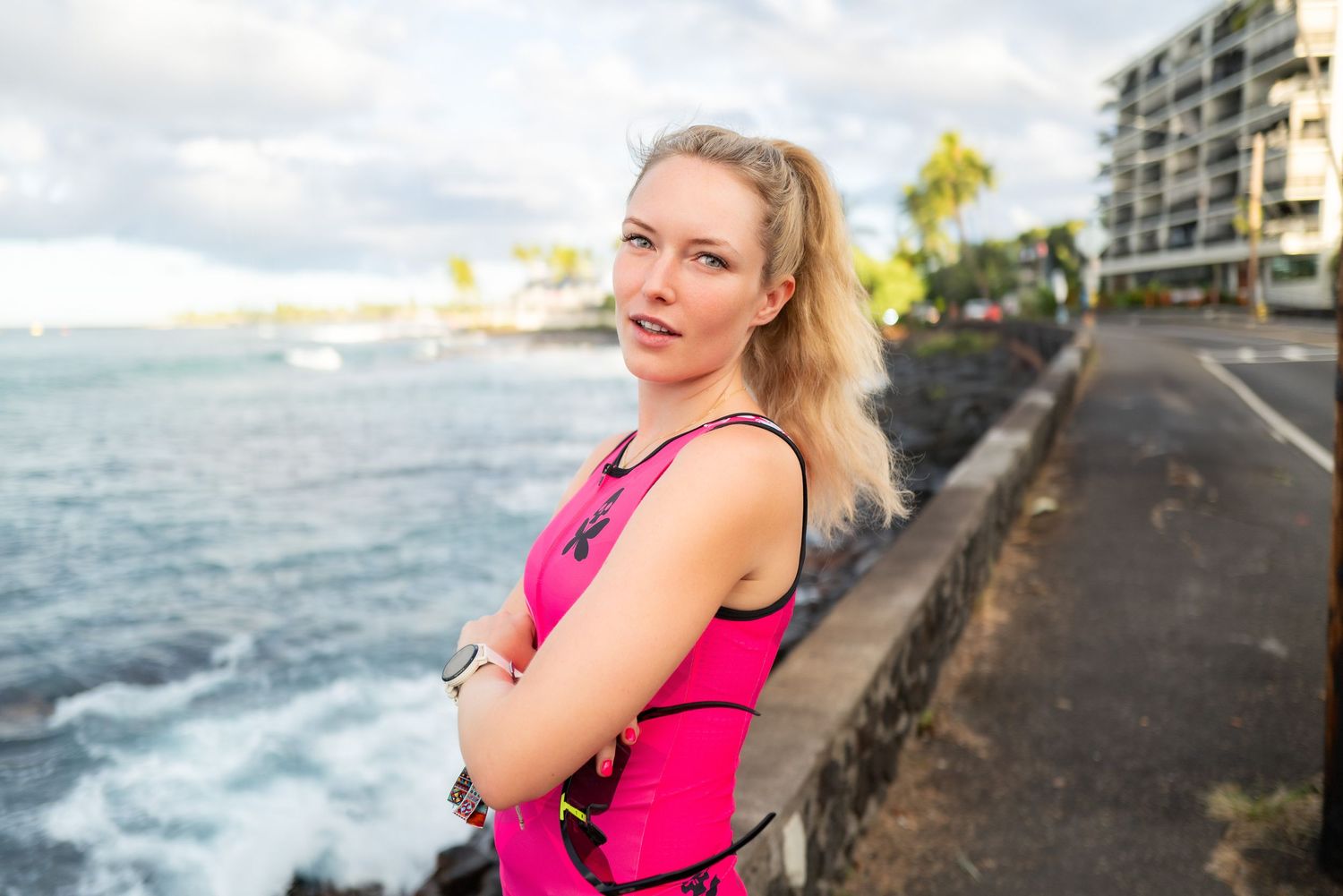 Blonde woman in pink athletic top standing by ocean wall in Hawaii.