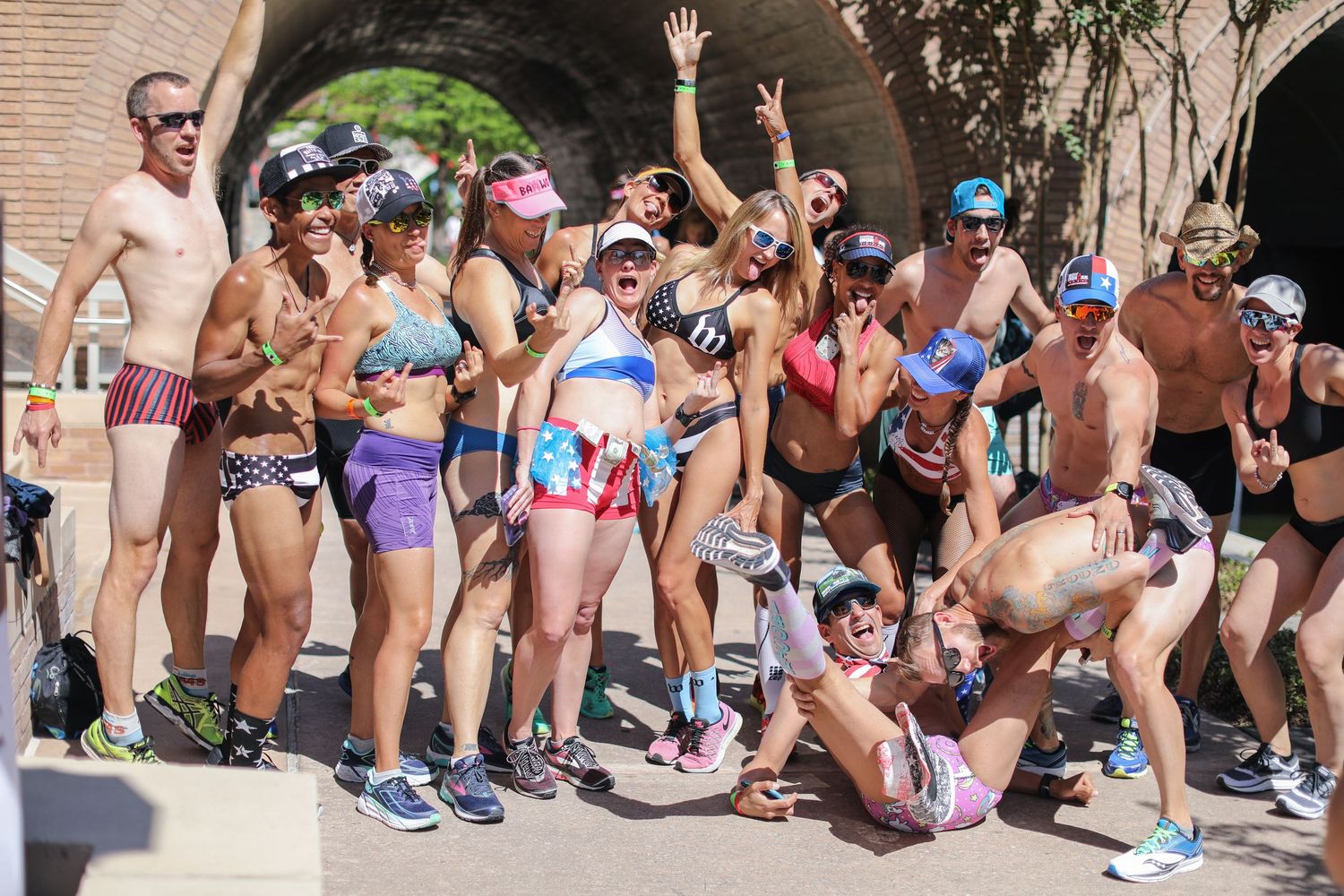 Large group of triathlon participants in swimwear and goggles celebrating at the IMTX Underpants Run before a race start.