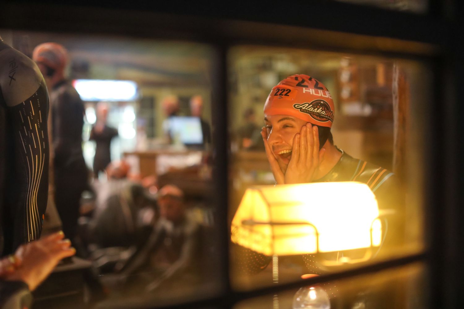 Athlete wearing orange headband reflects in restaurant window under warm lamp light.