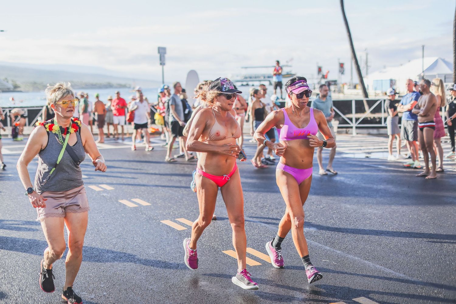 Three women in colorful athletic wear running together on a sunny street during the Kona Underpants Run.