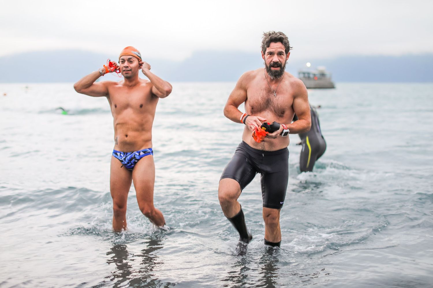 Two male swimmers emerge from open water during a triathlon or open water swim event.