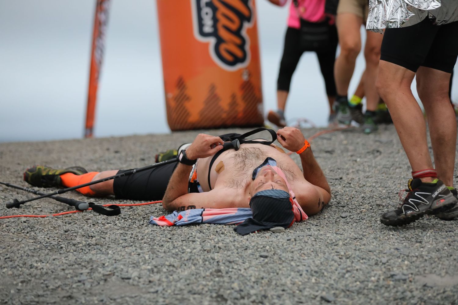 Exhausted triathlete lying on ground after completing Ironman race near finish banner.