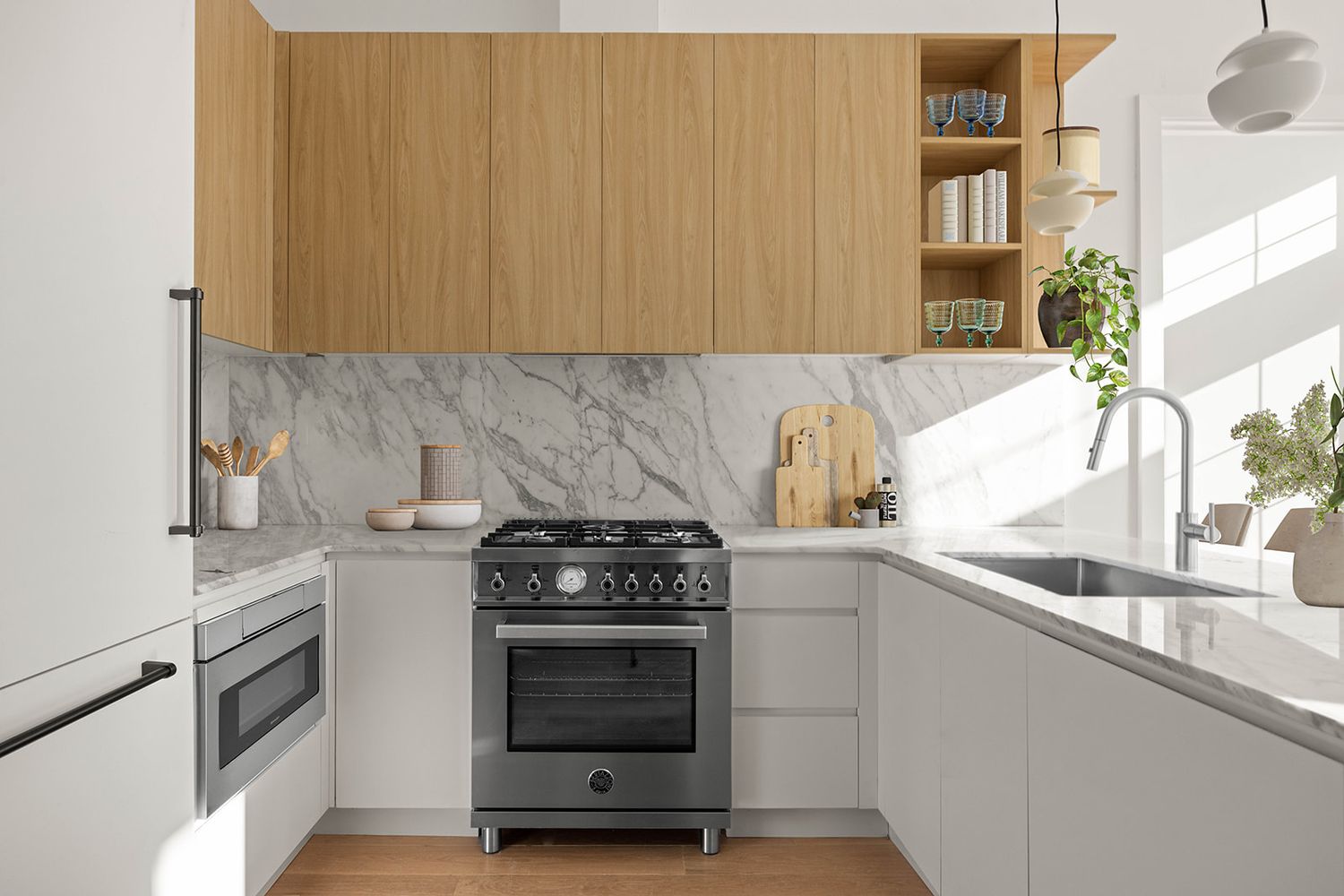 Modern kitchen with marble backsplash, black range stove, wood upper cabinets, and white lower cabinets on hardwood floors.
