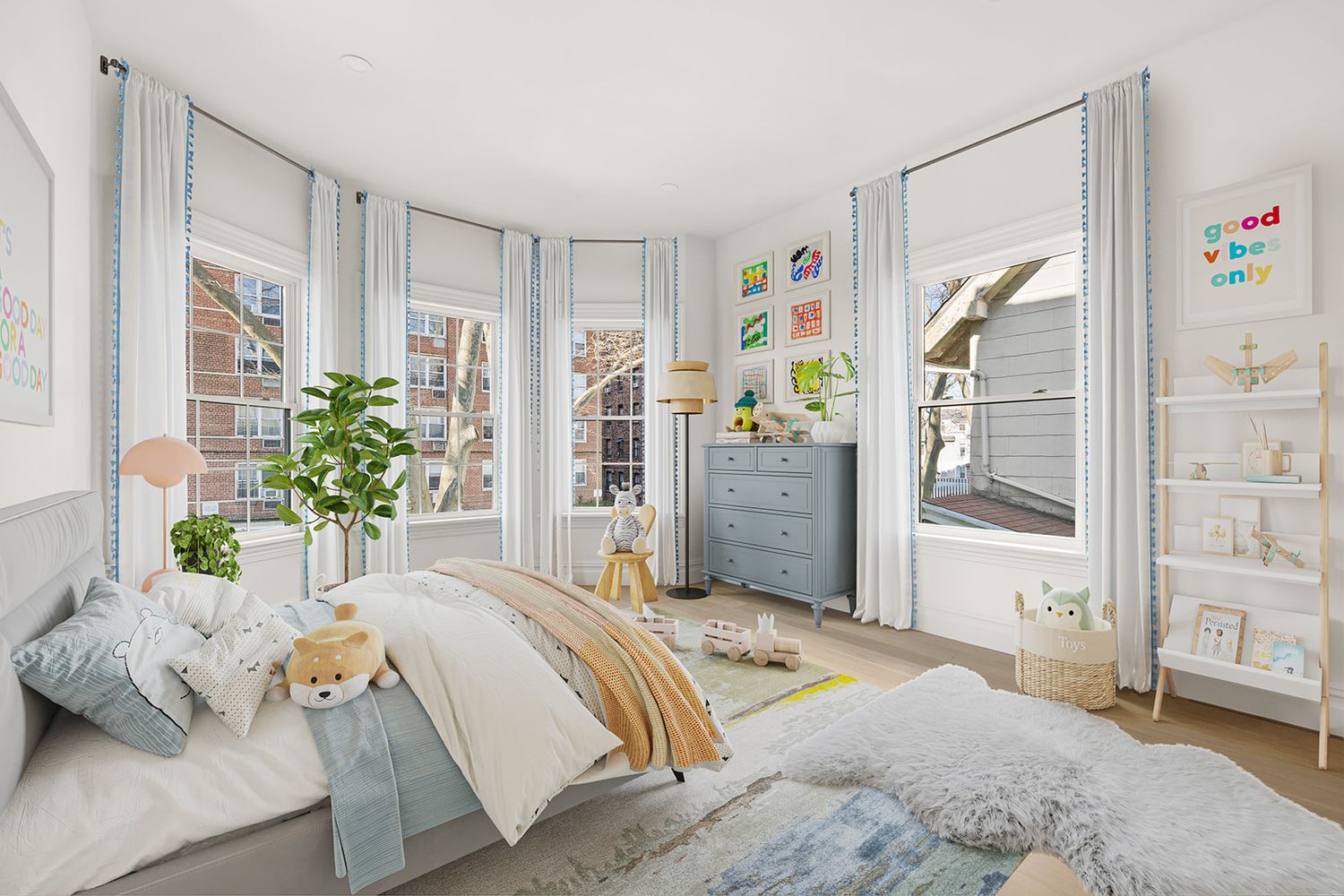 Bright children's bedroom with bay windows, light blue dresser, cozy bed with pastel bedding, and white bookshelves.