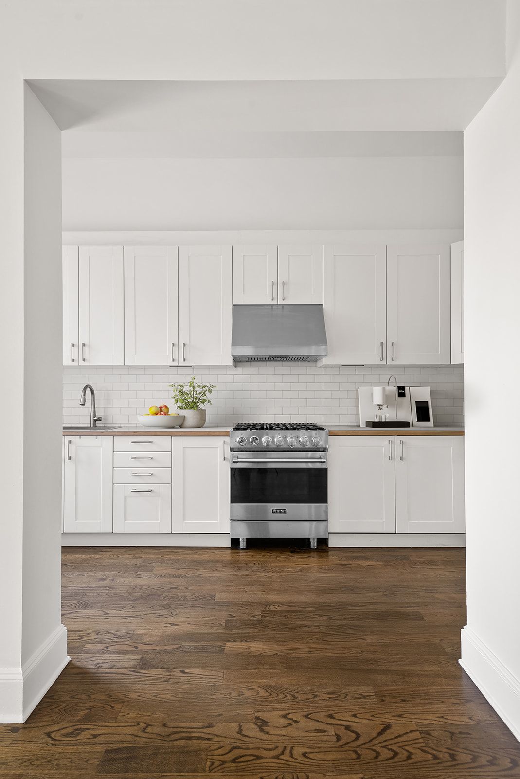 Modern white kitchen with shaker cabinets, butcher block counters, subway tile backsplash, and stainless steel range on hardwood floors.