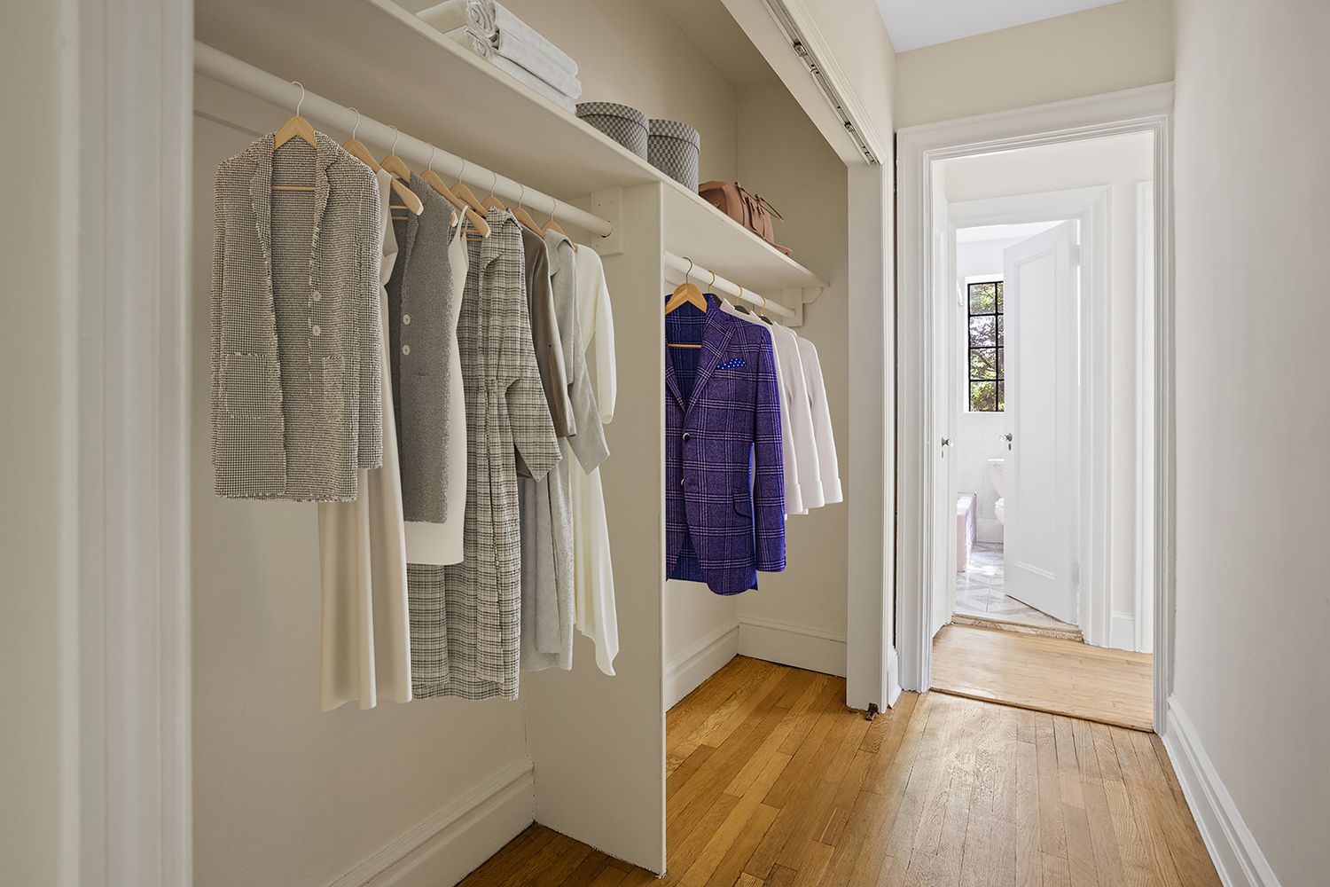 Open hallway closet with hanging clothes including a purple jacket, on hardwood floors in a bright home.
