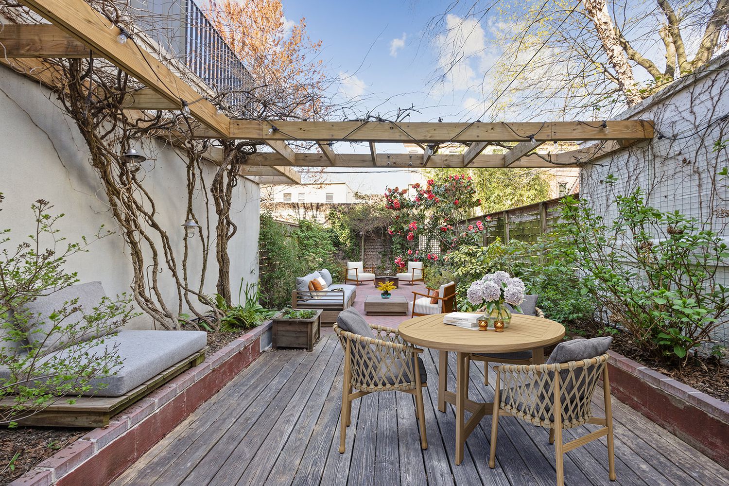 Charming outdoor deck with pergola, dining set, lounge seating, and lush climbing vines in a private garden patio.