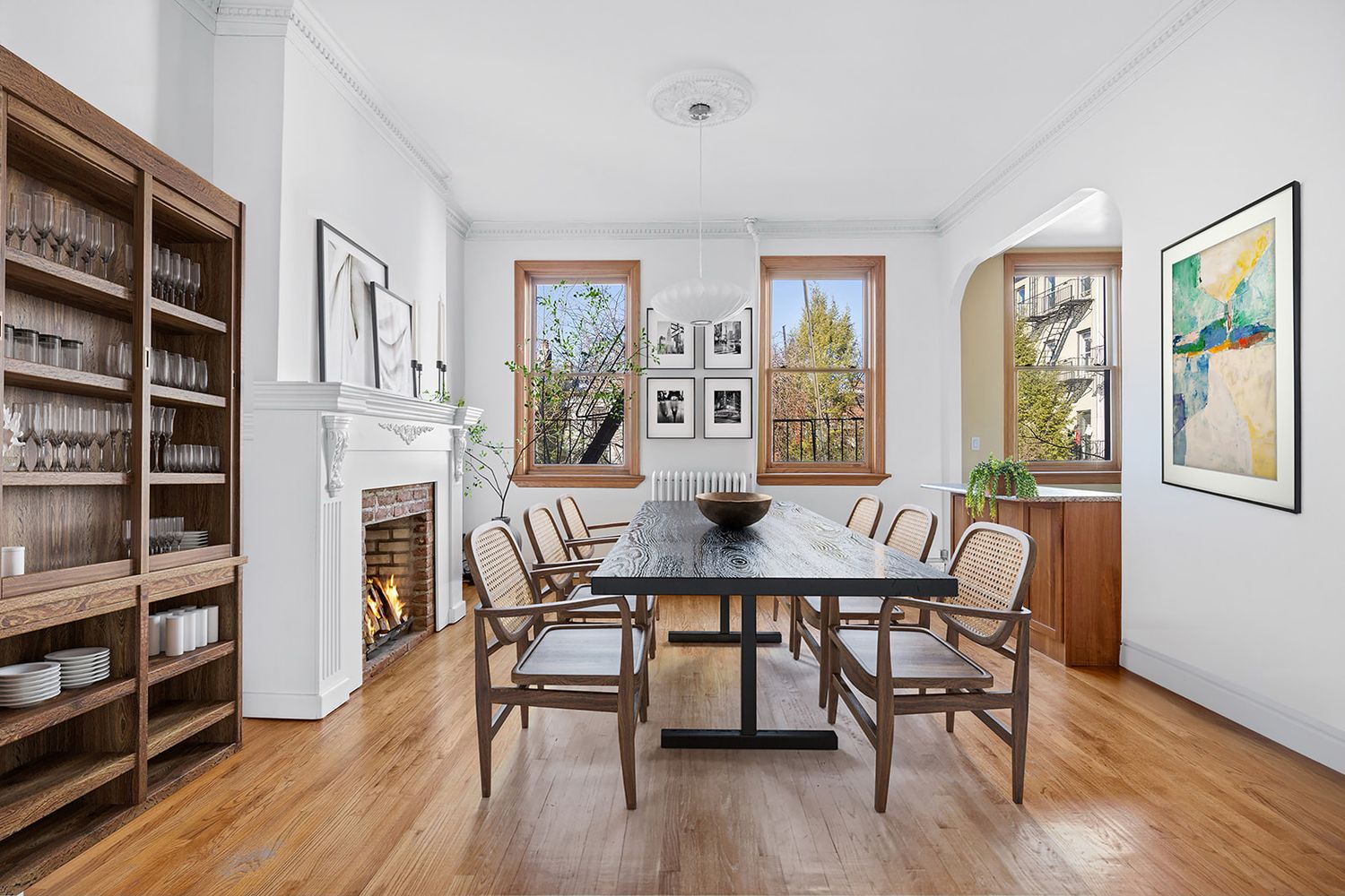 Elegant dining room with hardwood floors, wood dining set, built-in bookcase, fireplace, and arched doorway in natural light.