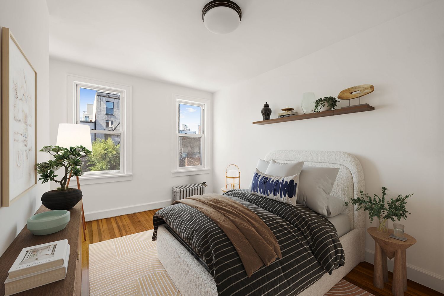 Bright bedroom with hardwood floors, floating shelf, two windows, and cozy striped bedding in a modern apartment.