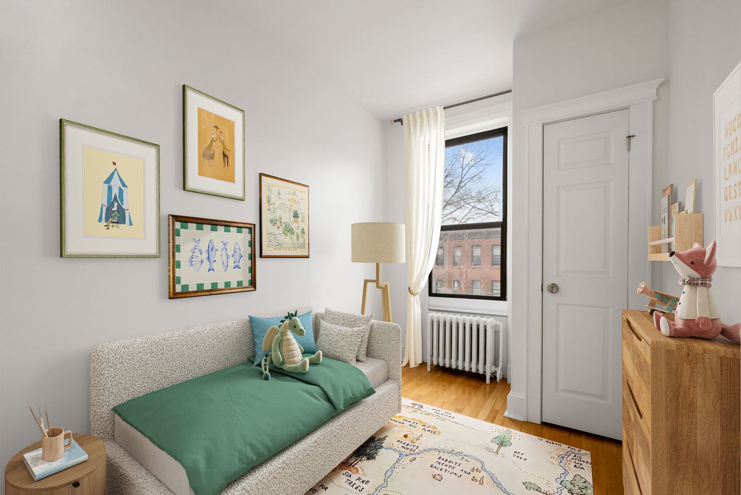 Bright child's bedroom with green daybed, framed artwork, hardwood floors, white radiator, and natural light from a large window.