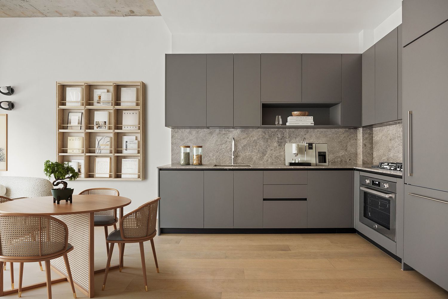Modern gray japandi kitchen with marble backsplash, built-in oven, and wooden dining set on light hardwood floors.