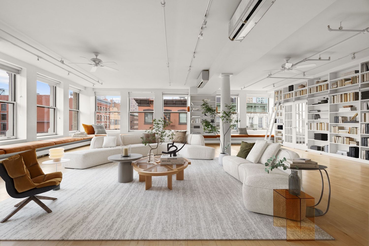 Bright, open-plan loft living room with white sofas, hardwood floors, built-in bookshelves, and large windows.