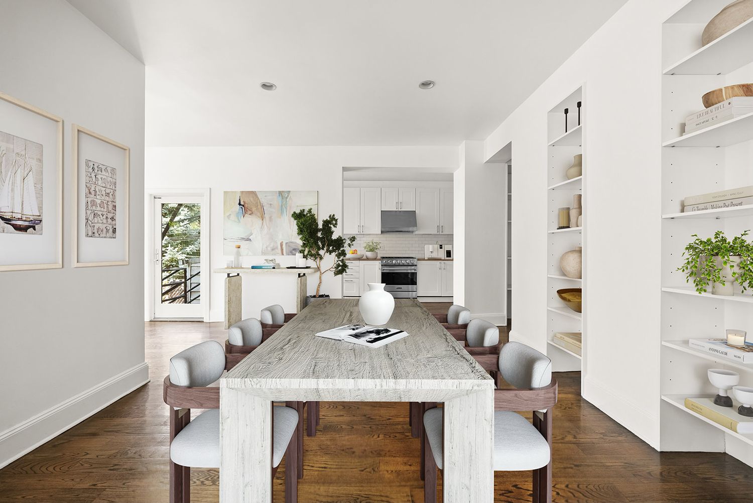 Modern open-plan dining room with marble table, upholstered chairs, built-in shelving, and white kitchen in background.