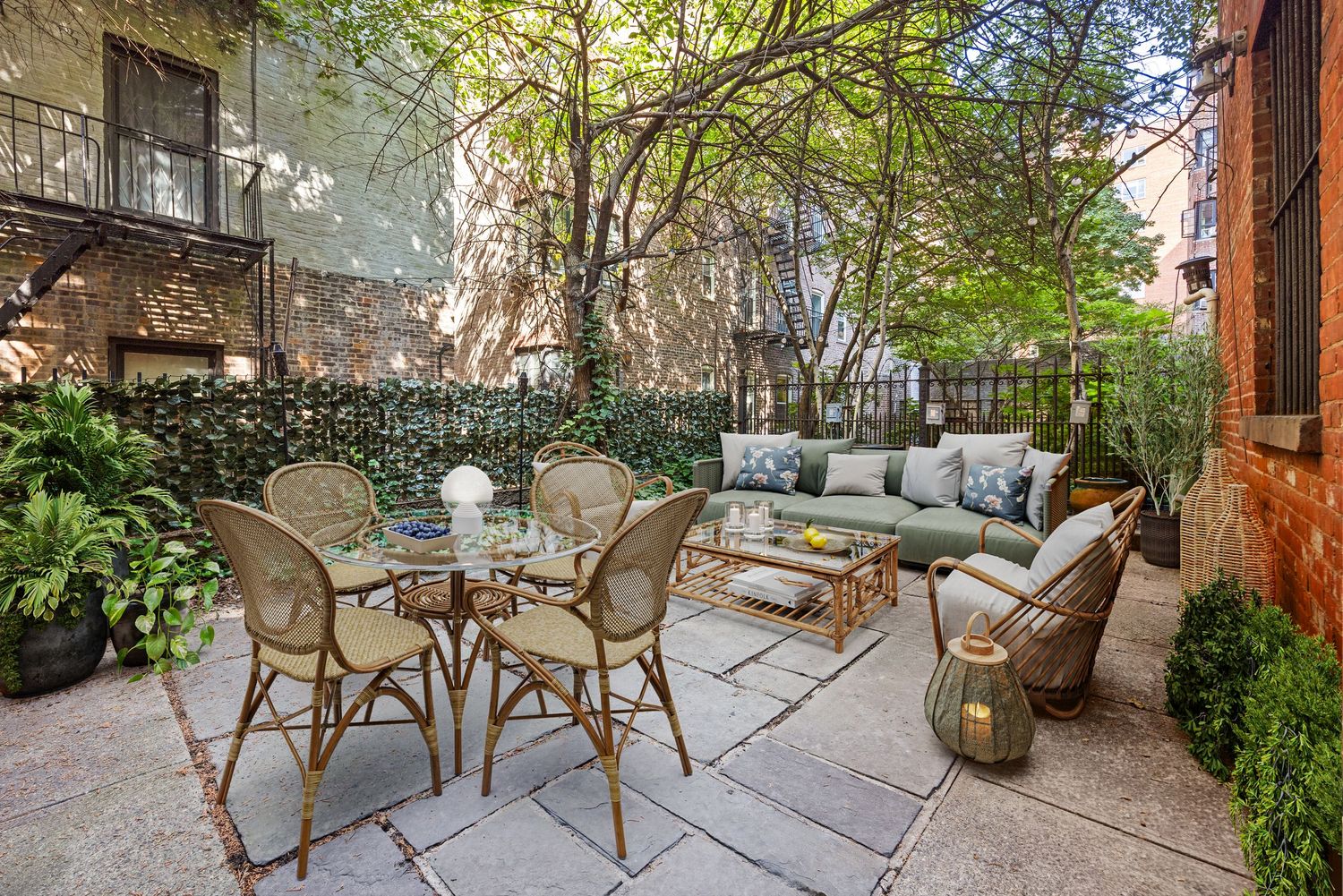 Charming outdoor patio with wicker furniture, lush greenery, and stone flooring in a cozy urban garden setting.