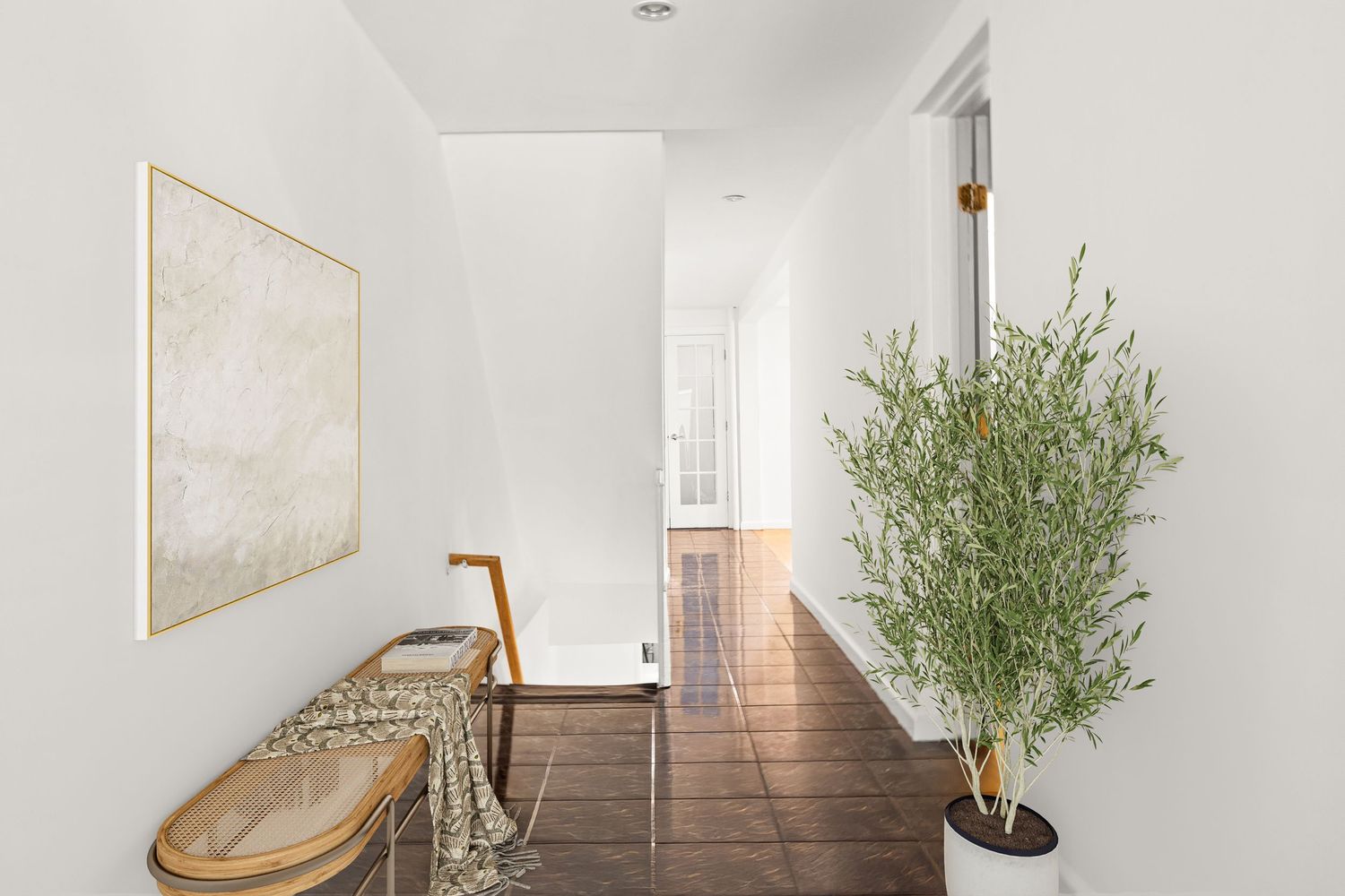 Minimalist hallway with dark tile floors, white walls, a wooden bench, abstract art, and a tall green potted plant.