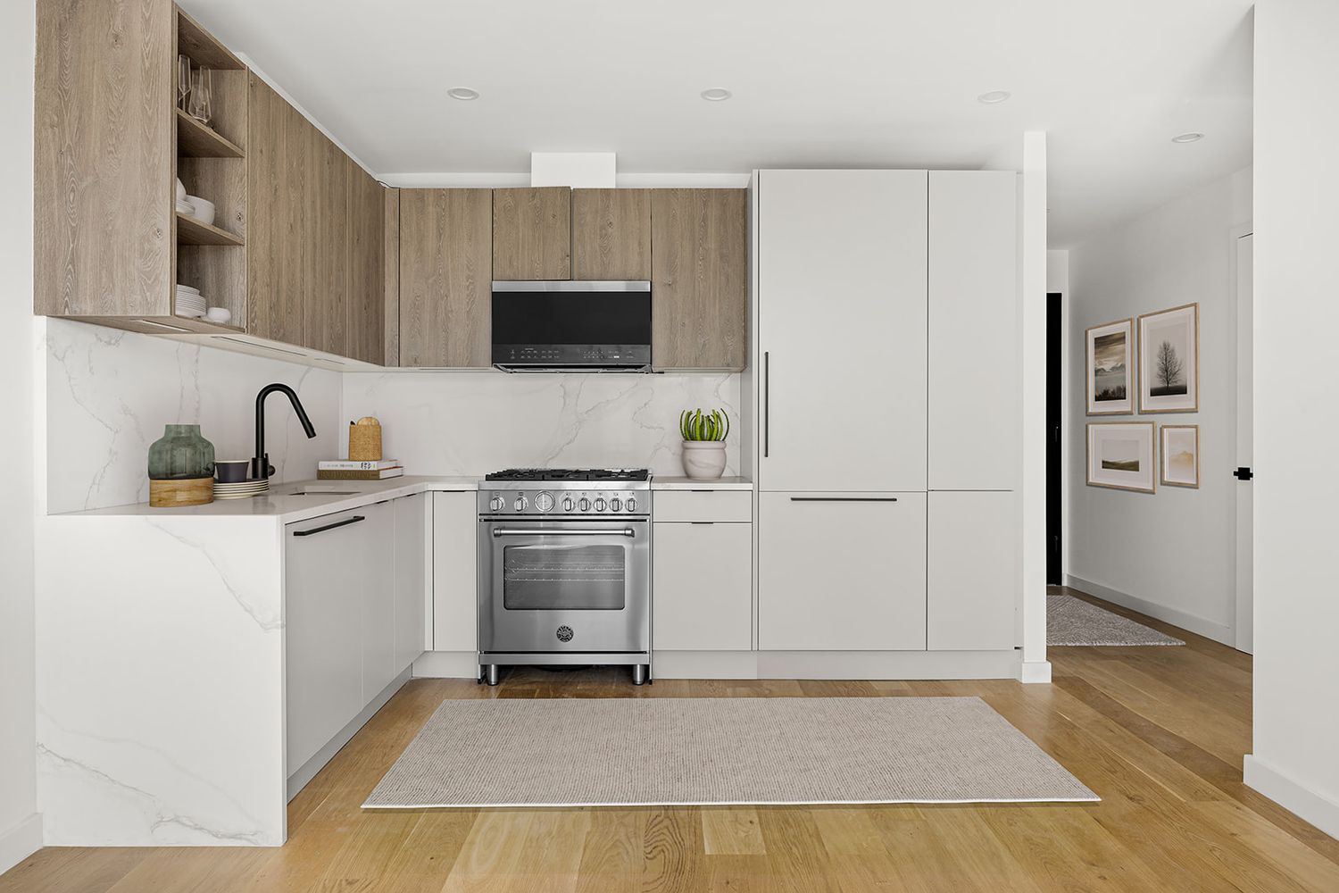 Modern kitchen with white cabinets, wood upper shelves, stainless steel range, marble countertops, and light hardwood floors.