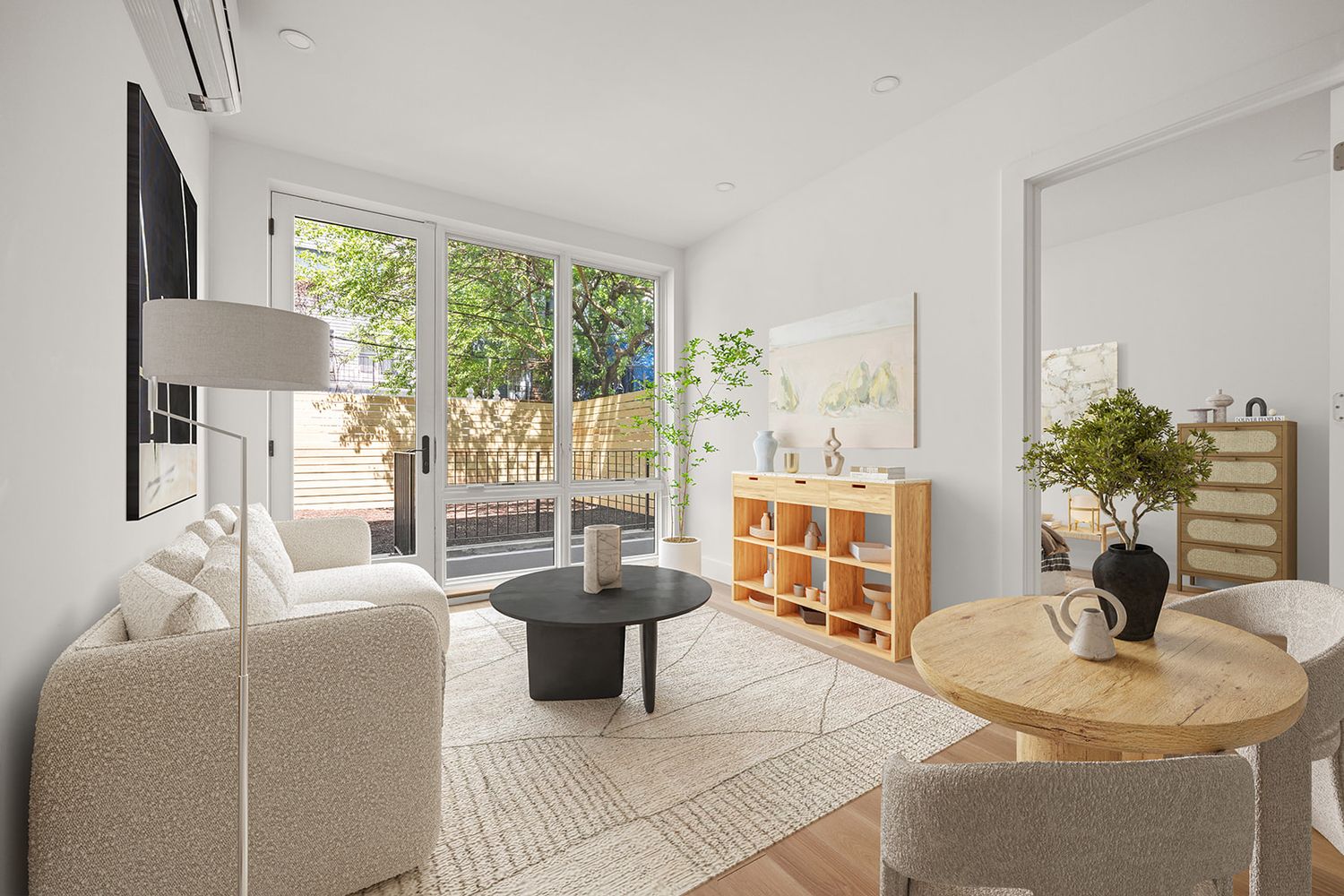 Bright modern living room with white sofa, round black coffee table, sliding glass doors to patio, and warm wood accents.