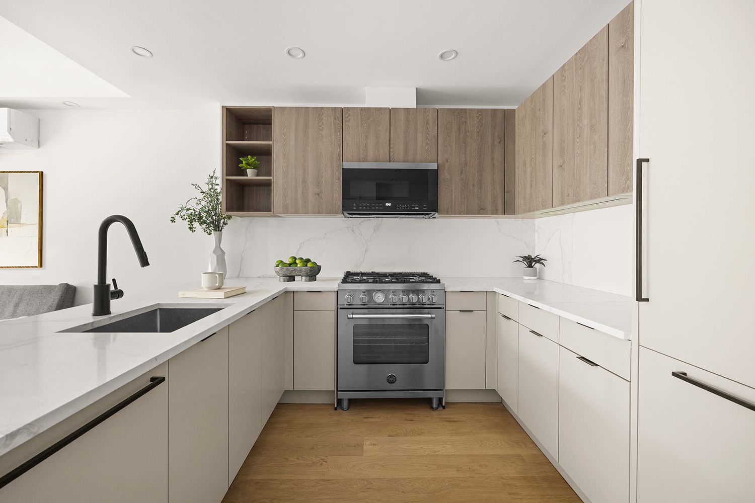 Modern kitchen with light wood upper cabinets, white lower cabinets, quartz countertops, stainless steel range, and hardwood floors.