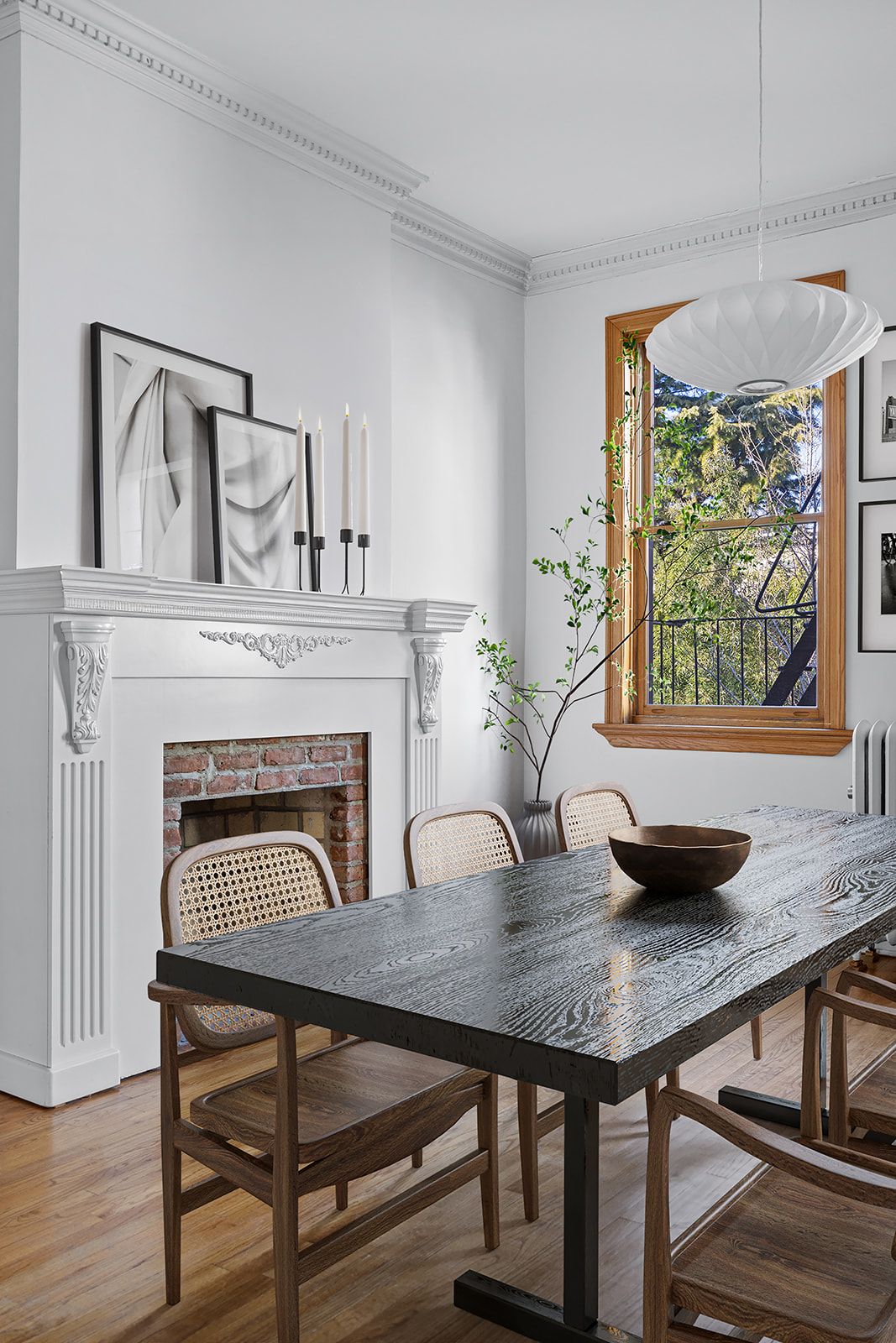Elegant dining room with dark marble table, cane chairs, white ornate fireplace, crown molding, and wood-framed window.