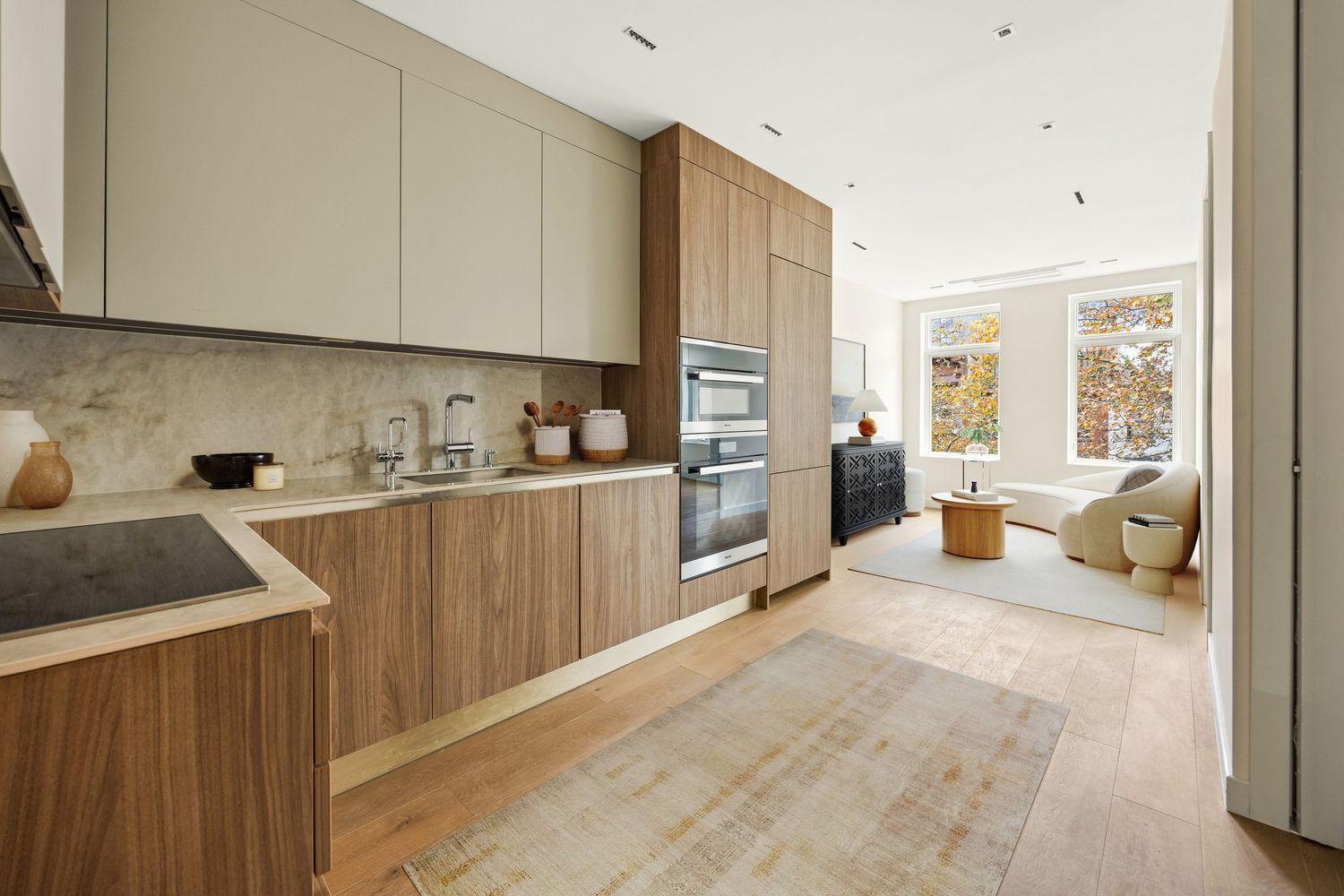 Modern kitchen with walnut cabinets, built-in ovens, stone backsplash, and open plan living area with natural light.