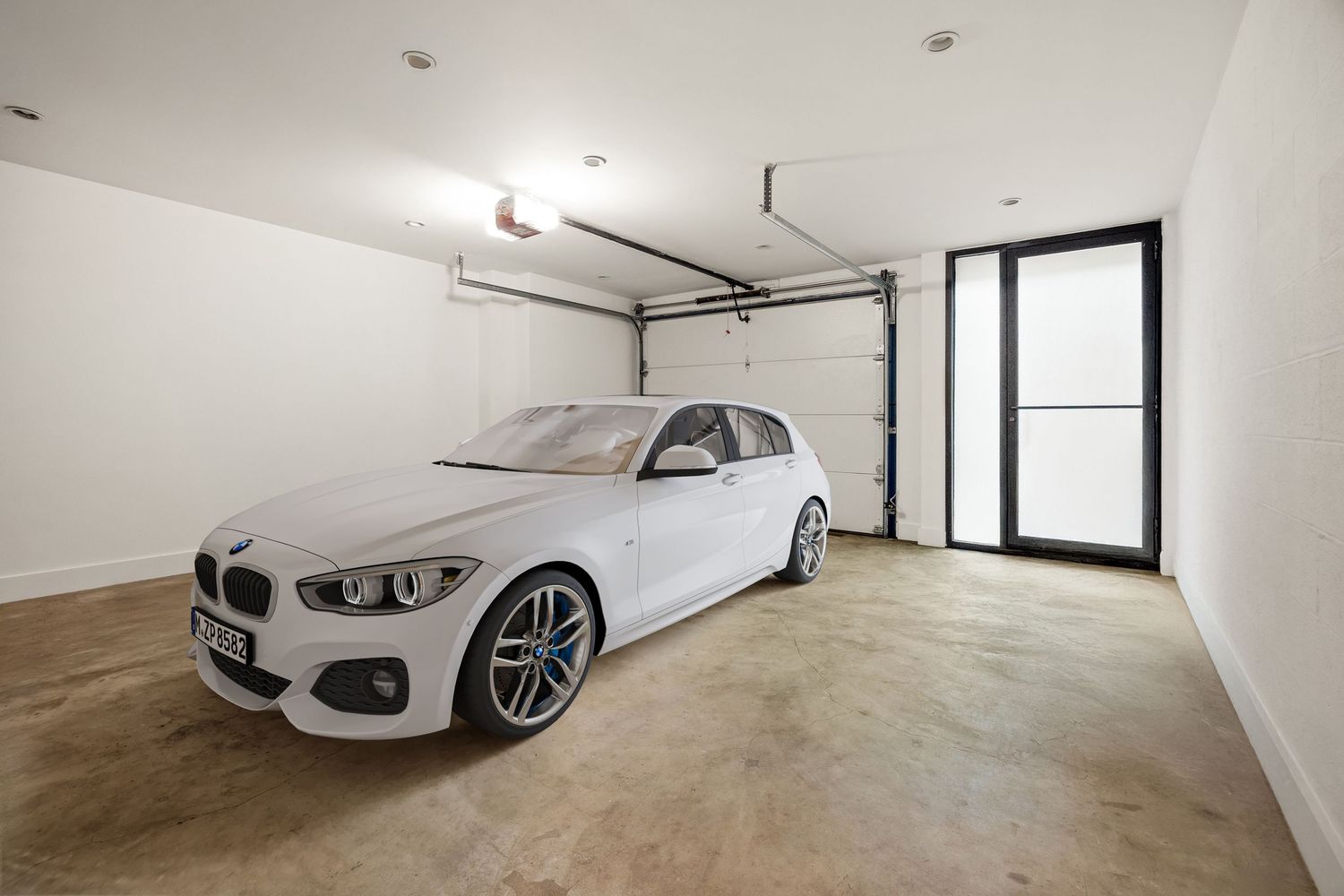 White BMW sedan parked inside a clean, spacious garage with concrete floors and a large window door.
