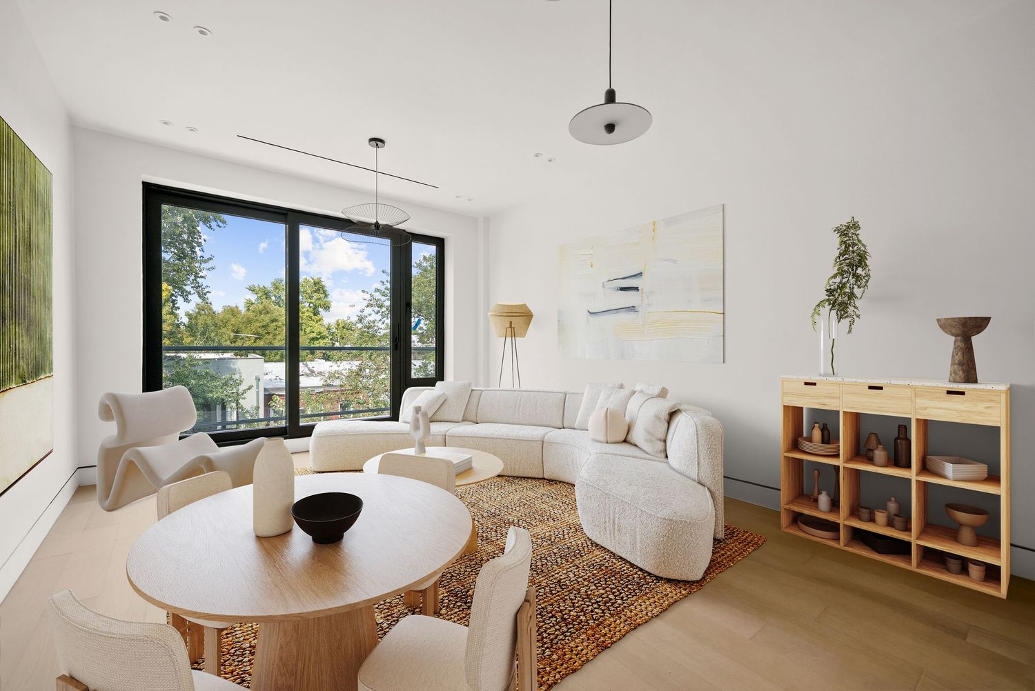 Modern living room with white sectional sofa, round dining table, hardwood floors, and large floor-to-ceiling windows with garden view.