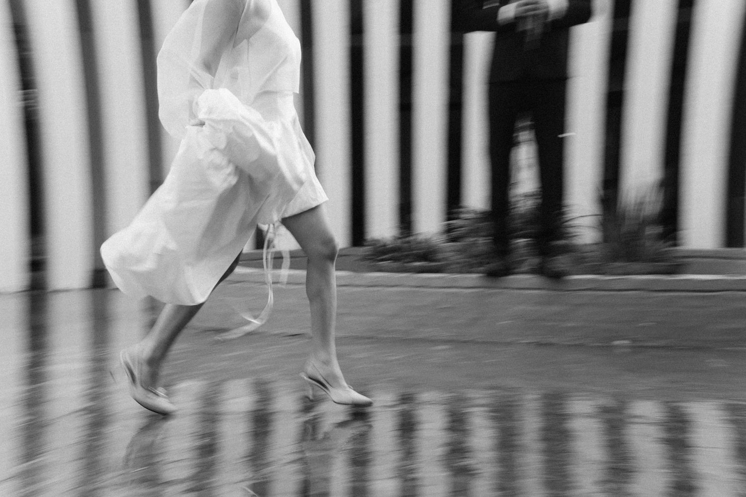 Black and white motion blur of a woman in a white dress running on a wet street.