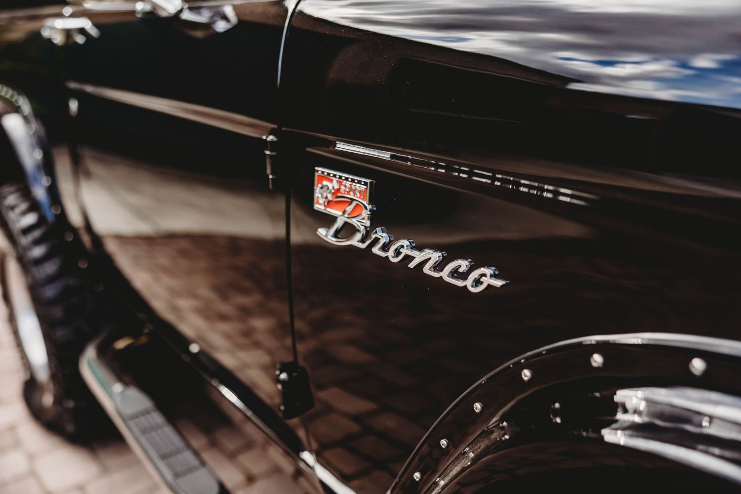 Close-up of classic Ford Bronco chrome emblem on shiny black vintage vehicle exterior.