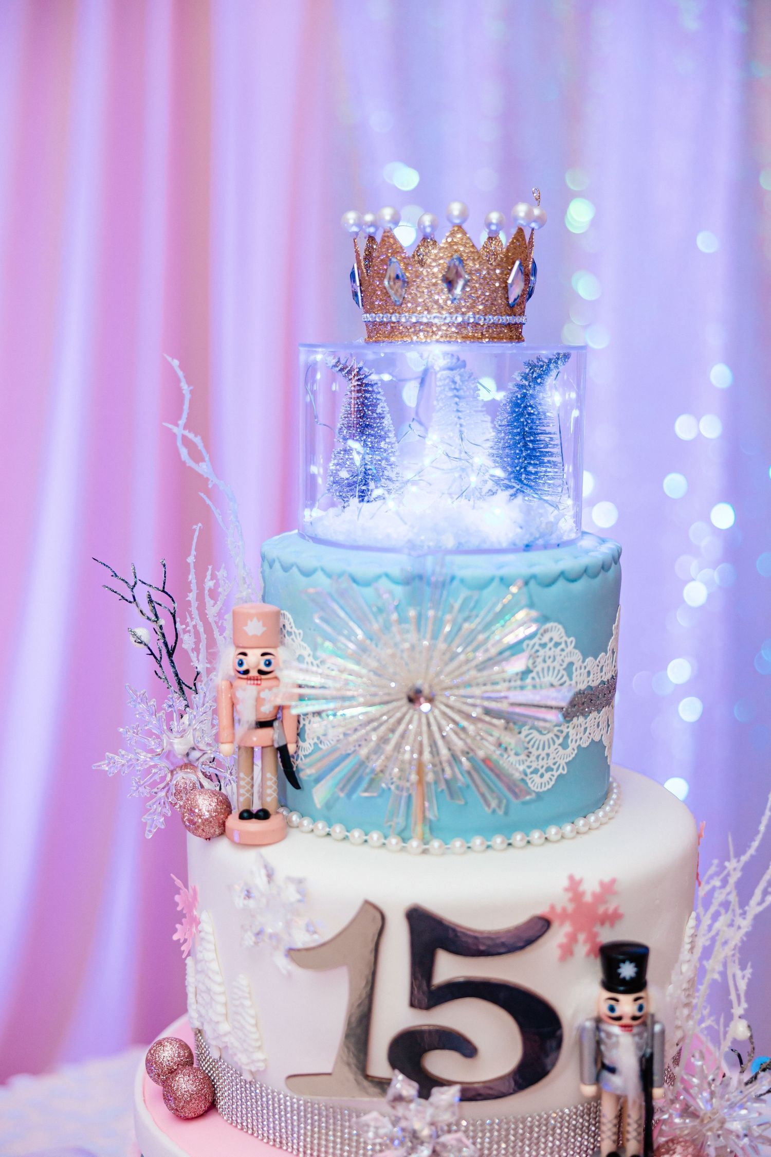 Elegant three-tier quinceañera cake with crown, nutcrackers, and snowflake decorations.